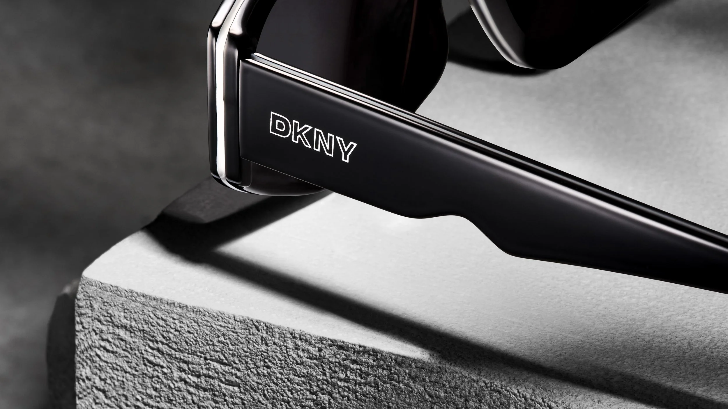 Close-up of a black DKNY-branded wristwatch resting on a textured white surface, with shadows cast on the surface.