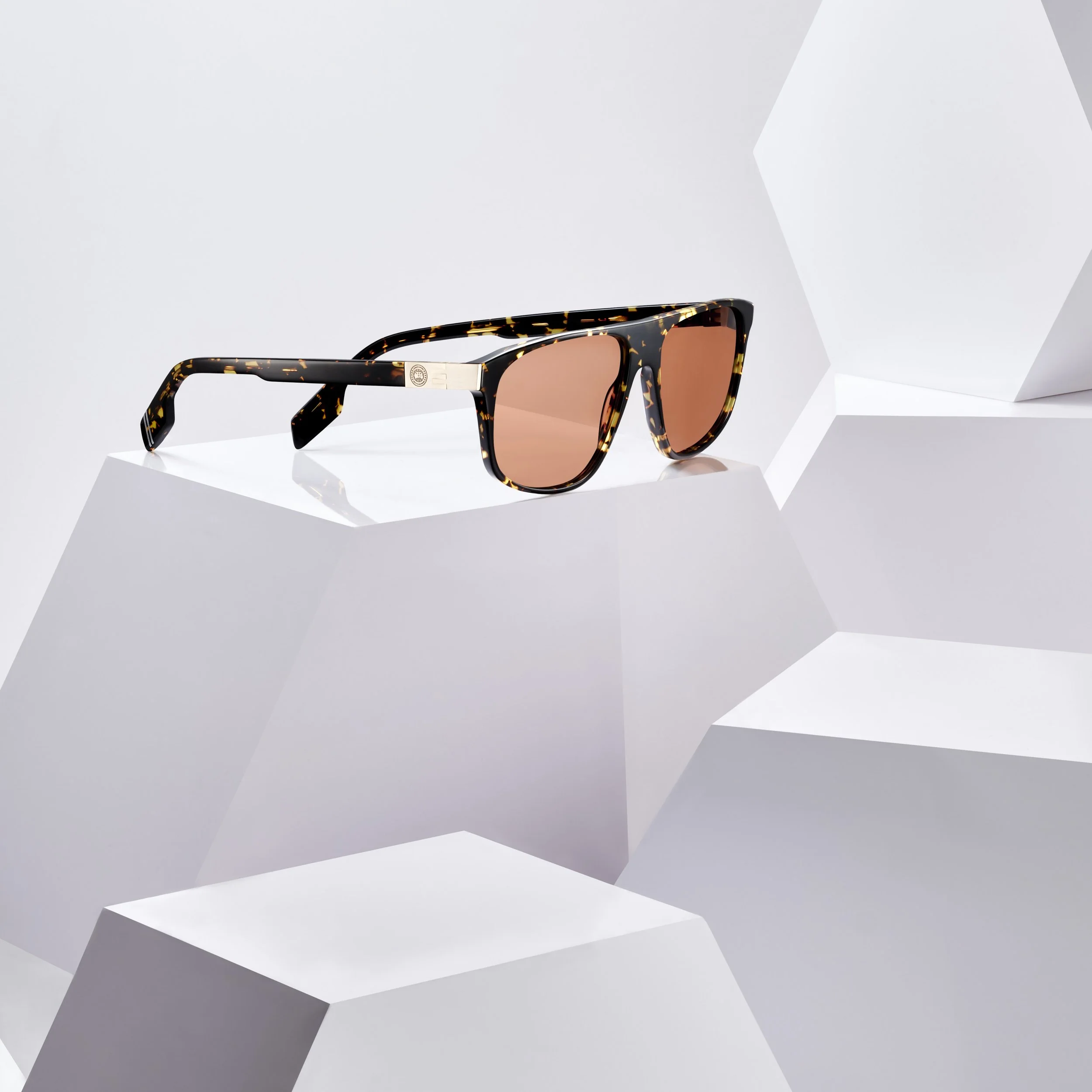 Tortoise shell sunglasses with pink tinted lenses on white geometric display