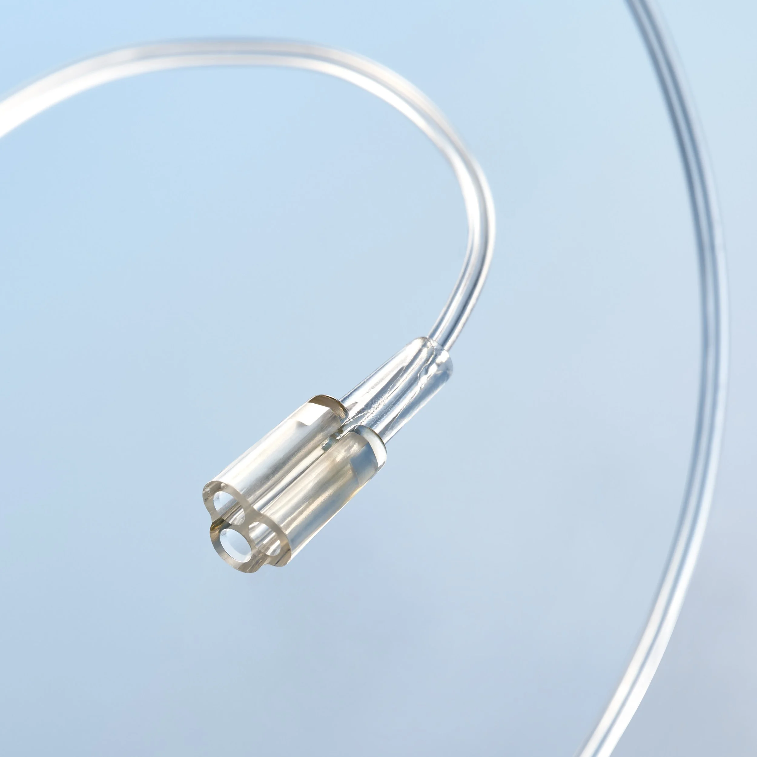 Close-up image of a clear medical catheter tube with a metallic connector, set against a light blue background.