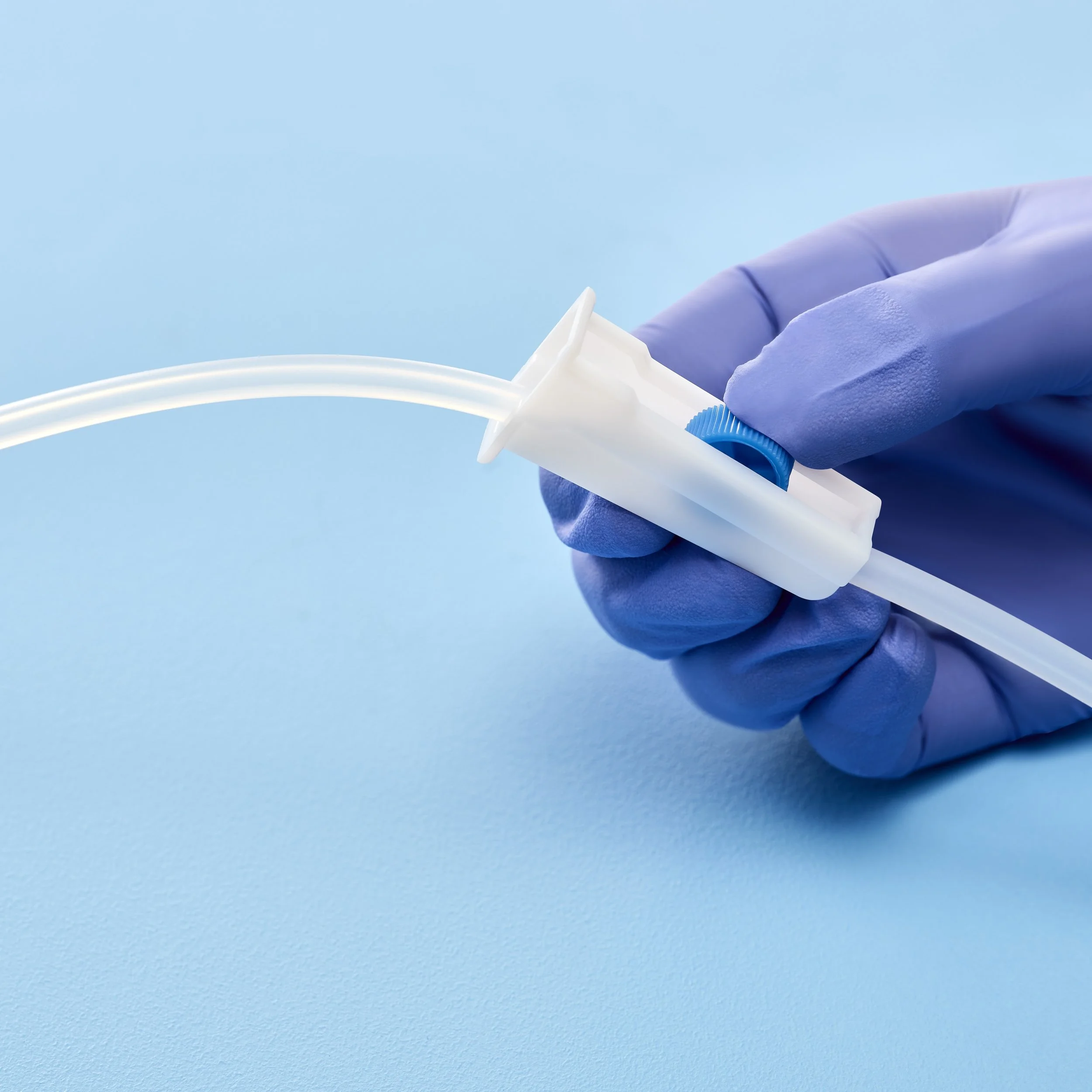 Close-up of a hand wearing a purple glove holding a medical device with a tube against a blue background.