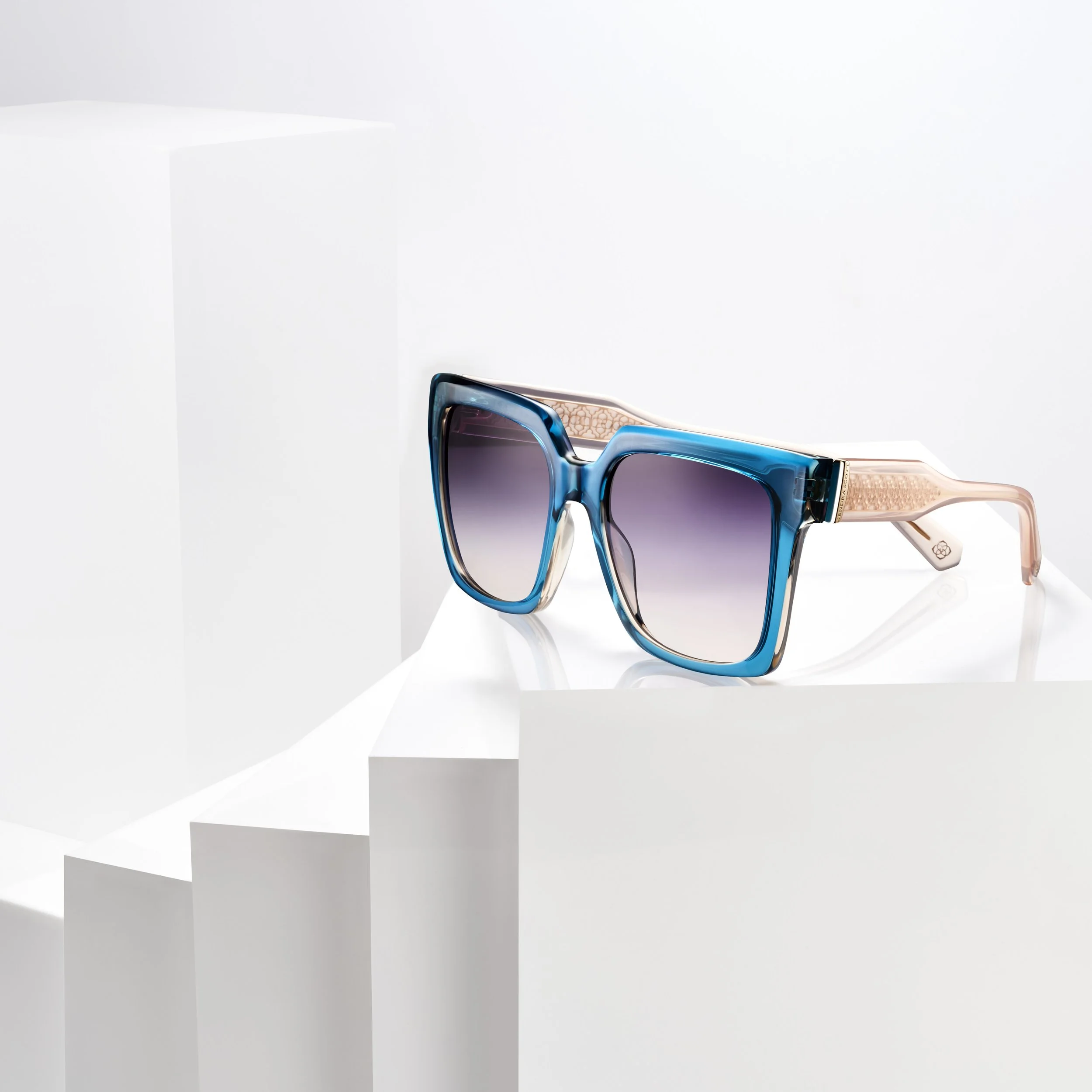 A pair of stylish sunglasses with blue frames and gradient lenses, resting on white geometric platforms.