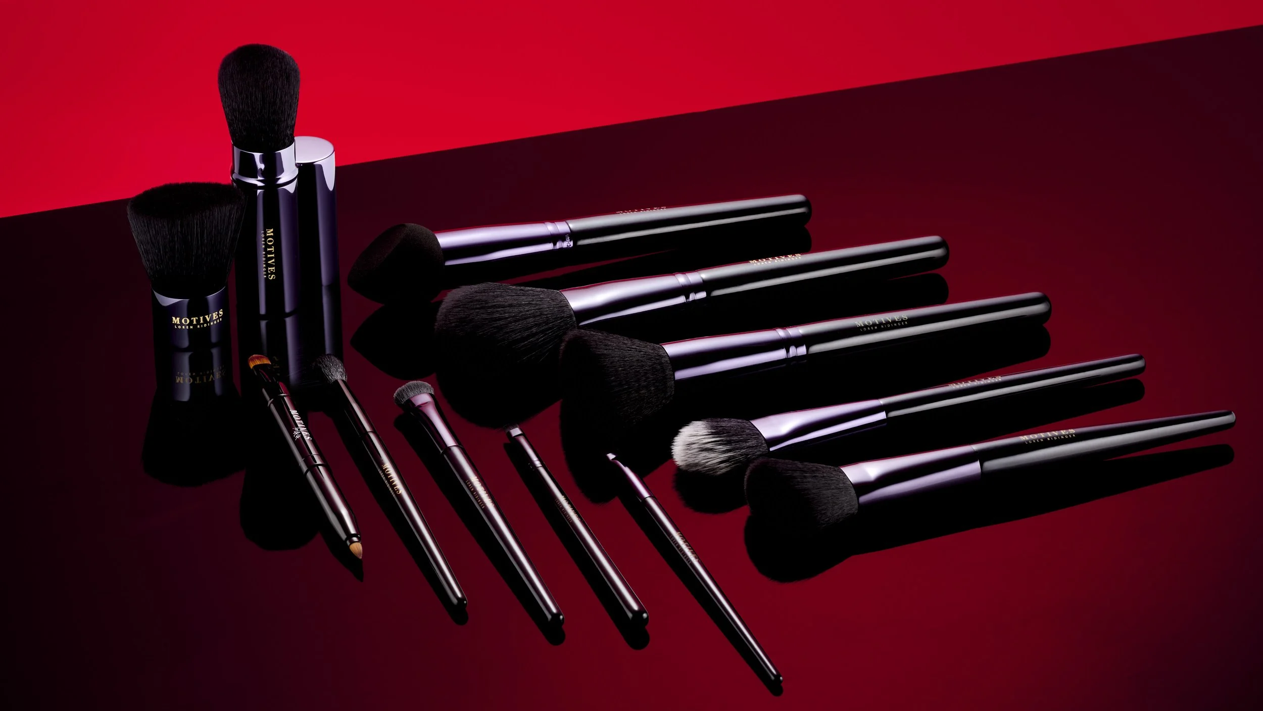 Set of black makeup brushes of various sizes and shapes with silver handles on a red and black background.