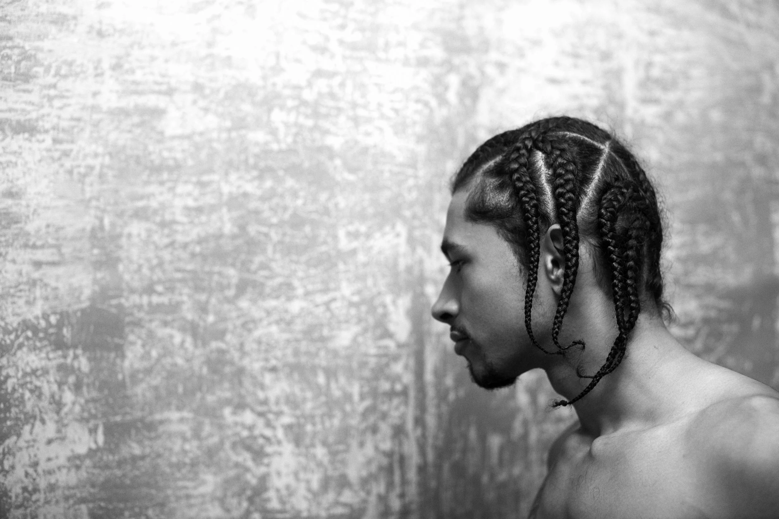 Side profile of a young woman with braided hair against a textured wall, in black and white.