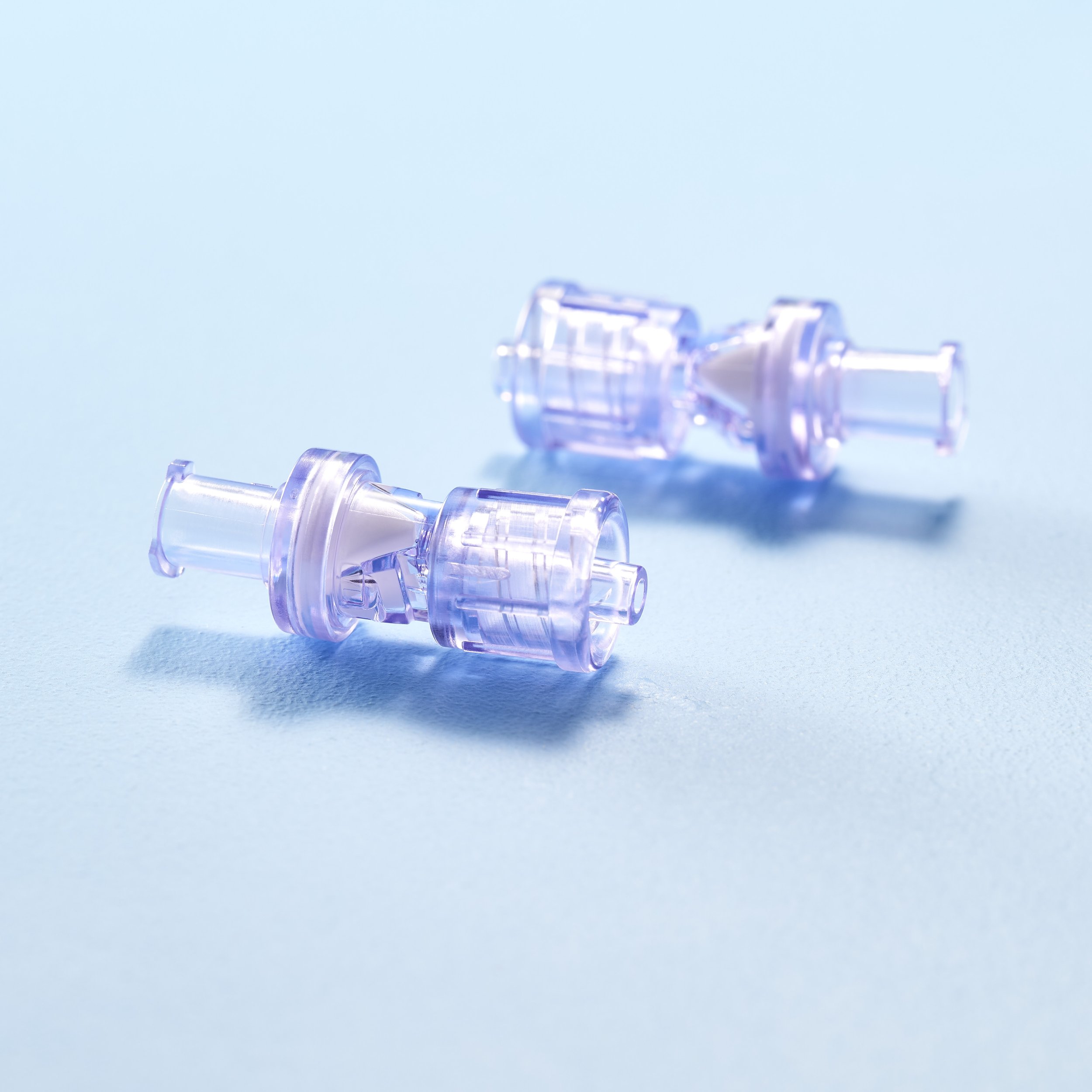 Two clear plastic medical syringes on a light blue background.