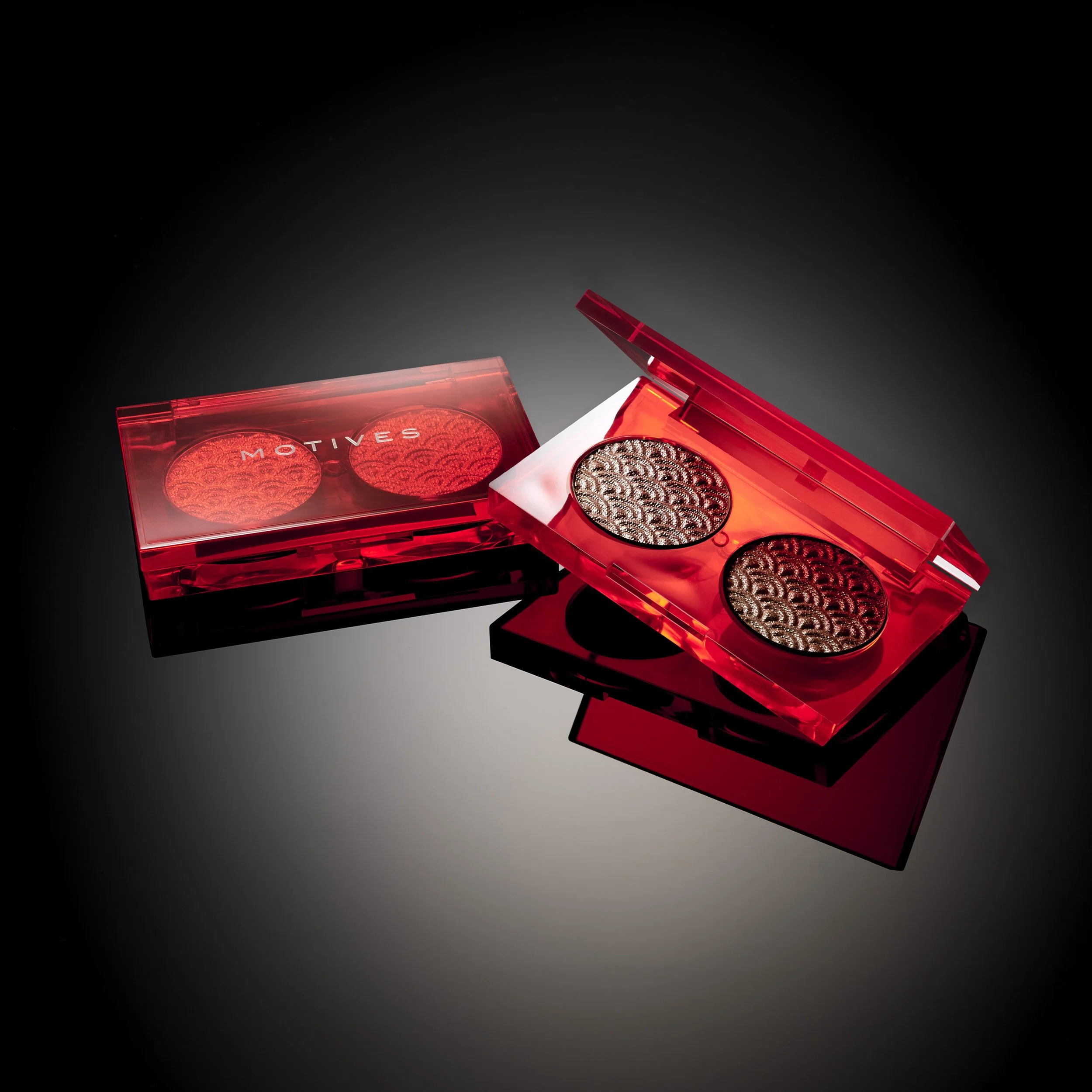 Two red makeup compacts with decorative patterns inside; one is closed, the other open revealing two eyeshadow pans.