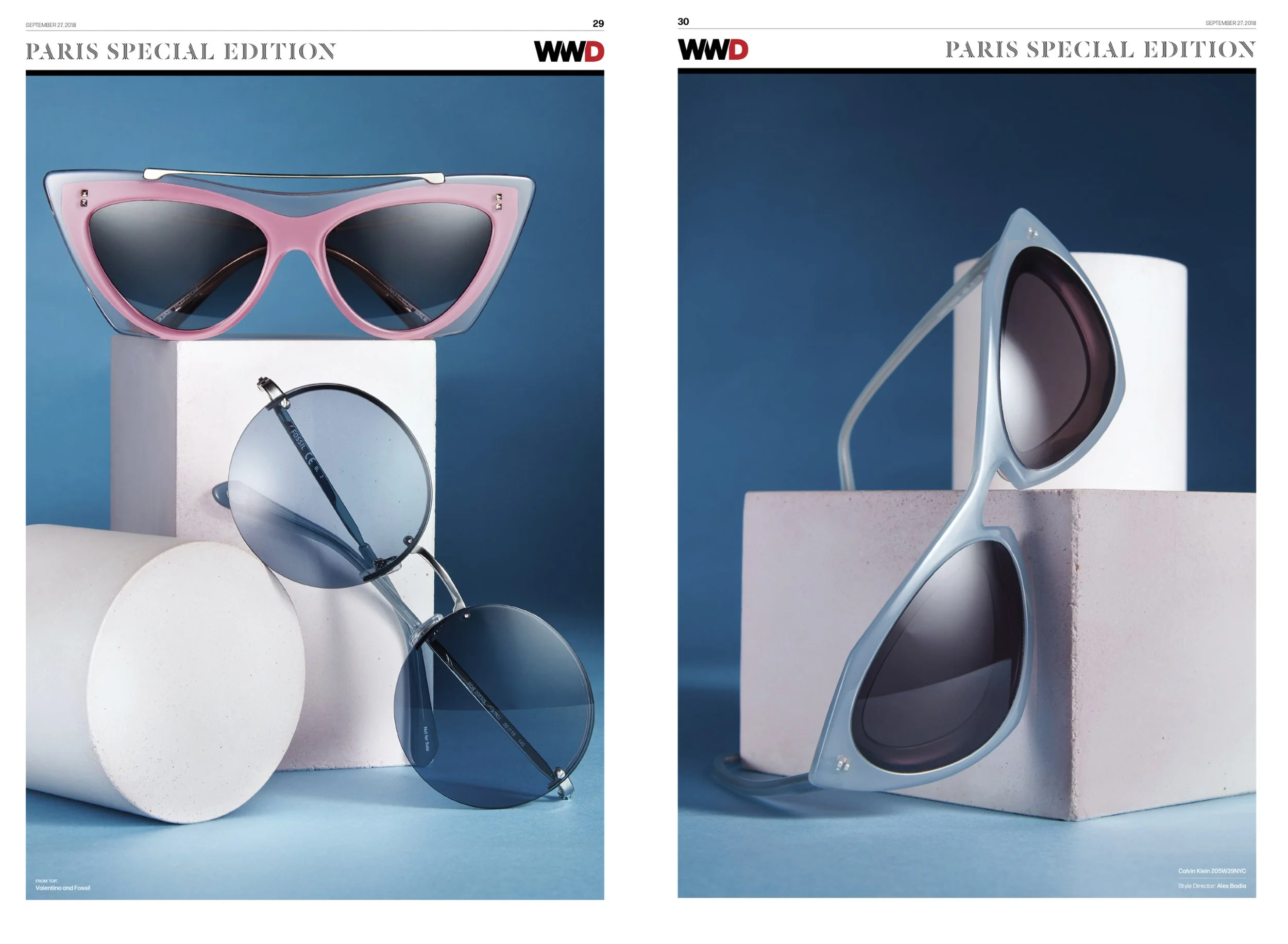 A pink pair of sunglasses with dark lenses on top of a white block, two blue-tinted sunglasses with circular lenses hanging on a white cylindrical object, and a pair of light blue sunglasses with dark lenses resting on a pink block, all against a blu
