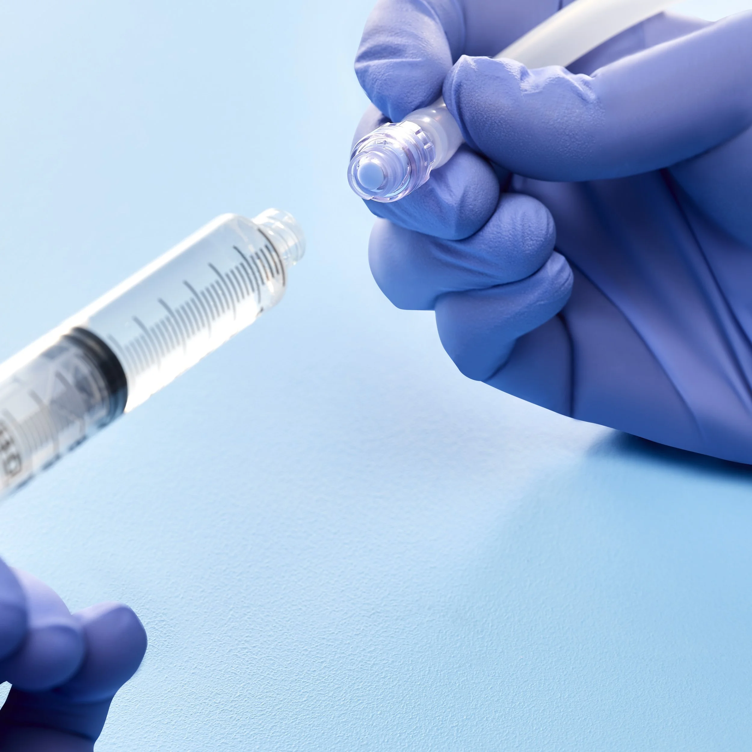 Hands in blue gloves holding a vaccine vial and syringe on a light blue background.