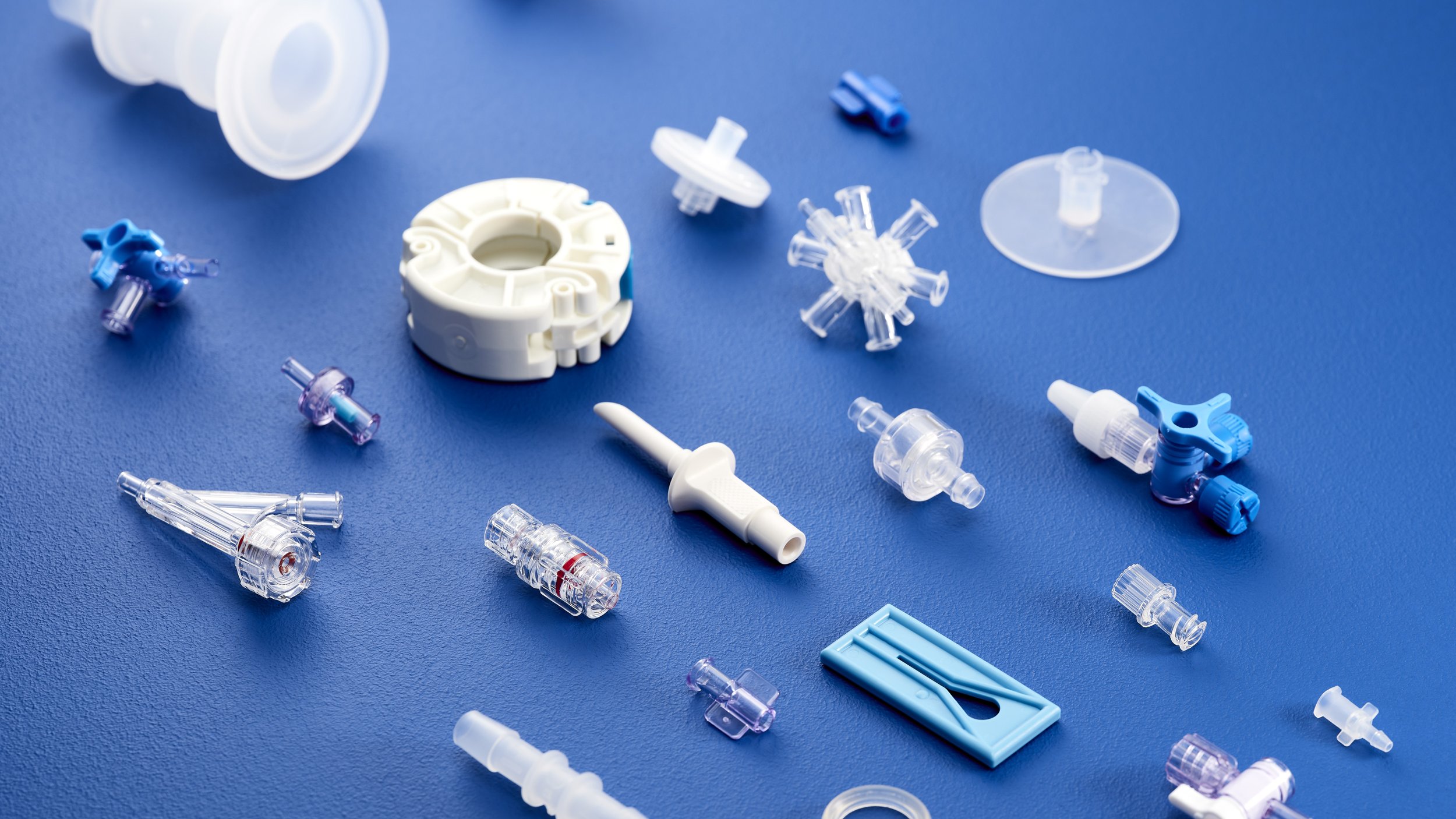 Various medical device components such as filters, connectors, and caps scattered on a blue surface.