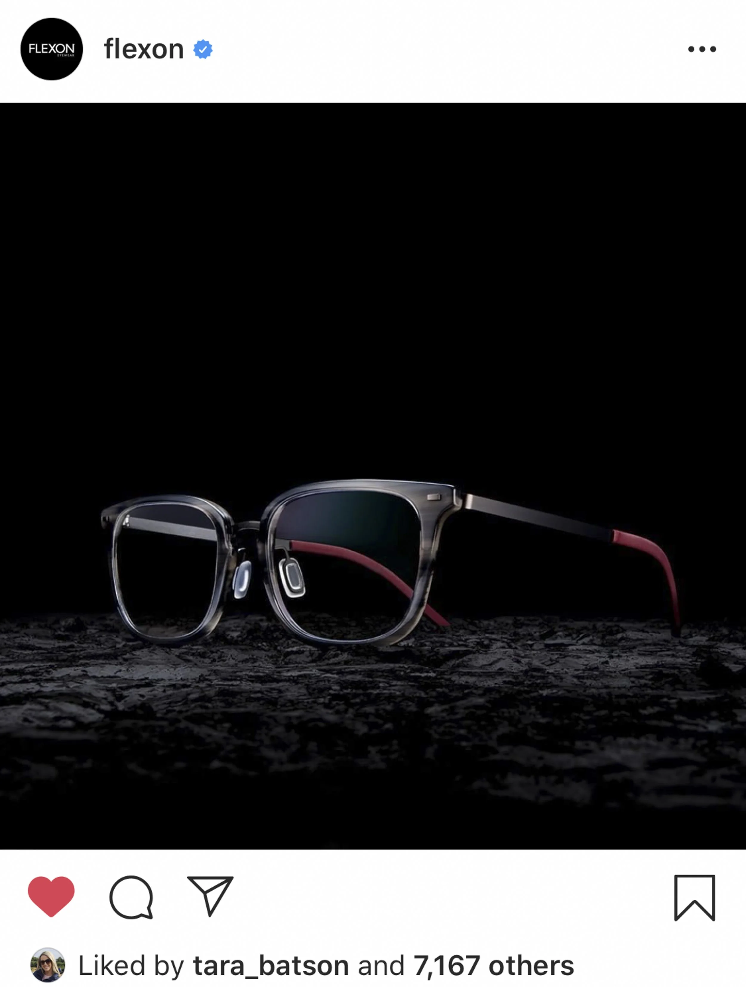 Black and gray eyeglasses with red accents placed on a textured black surface against a black background.
