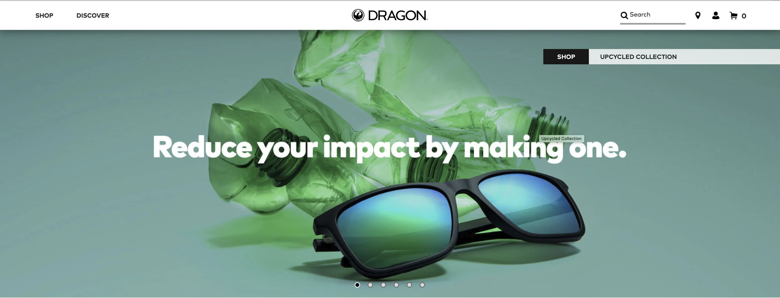 A pair of sunglasses with reflective blue-green lenses and black frames, resting on a light green surface with crumpled green plastic bottles in the background, promoting an upcycled collection to reduce environmental impact.