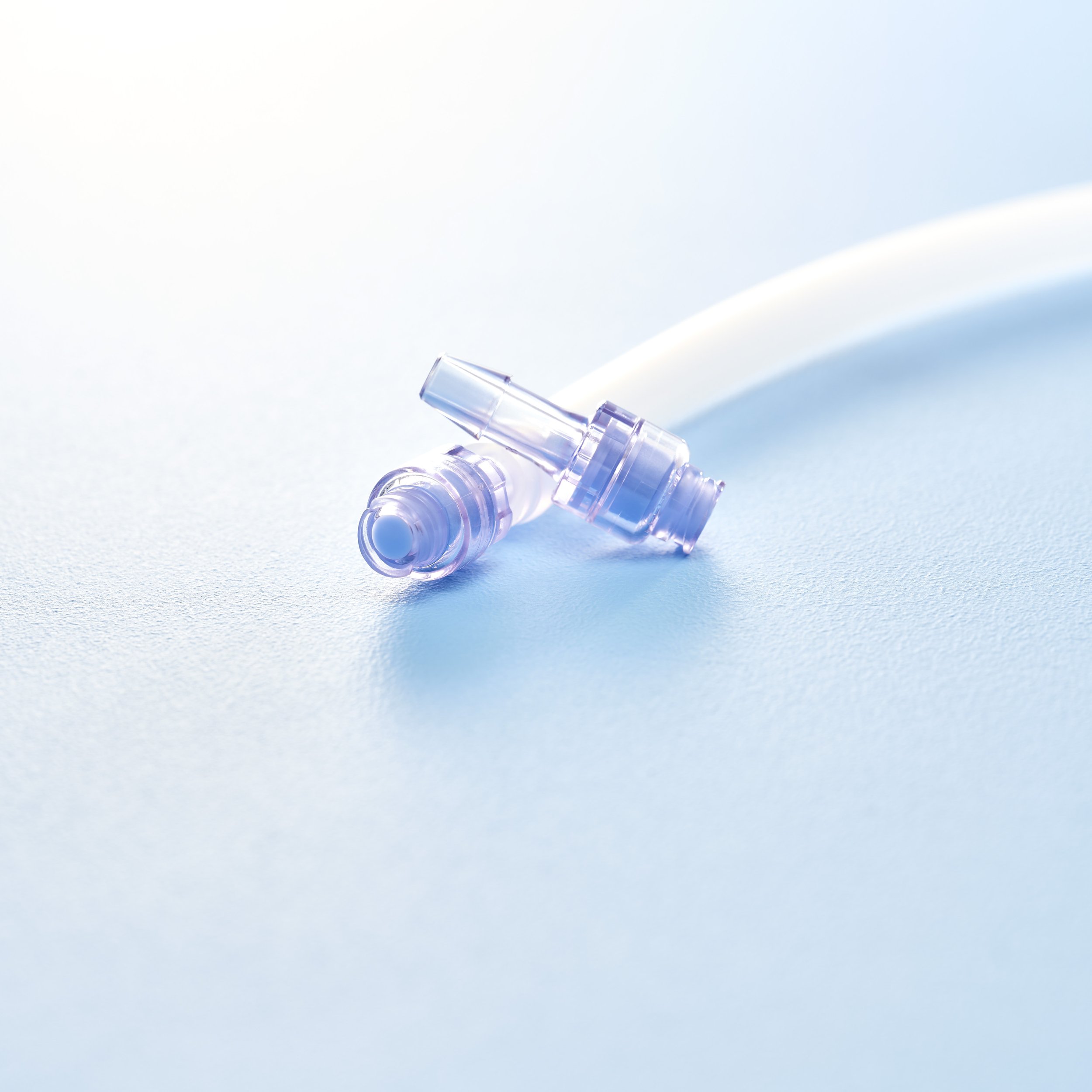 Close-up of two transparent earplugs on a blue surface with a white tube in the background.