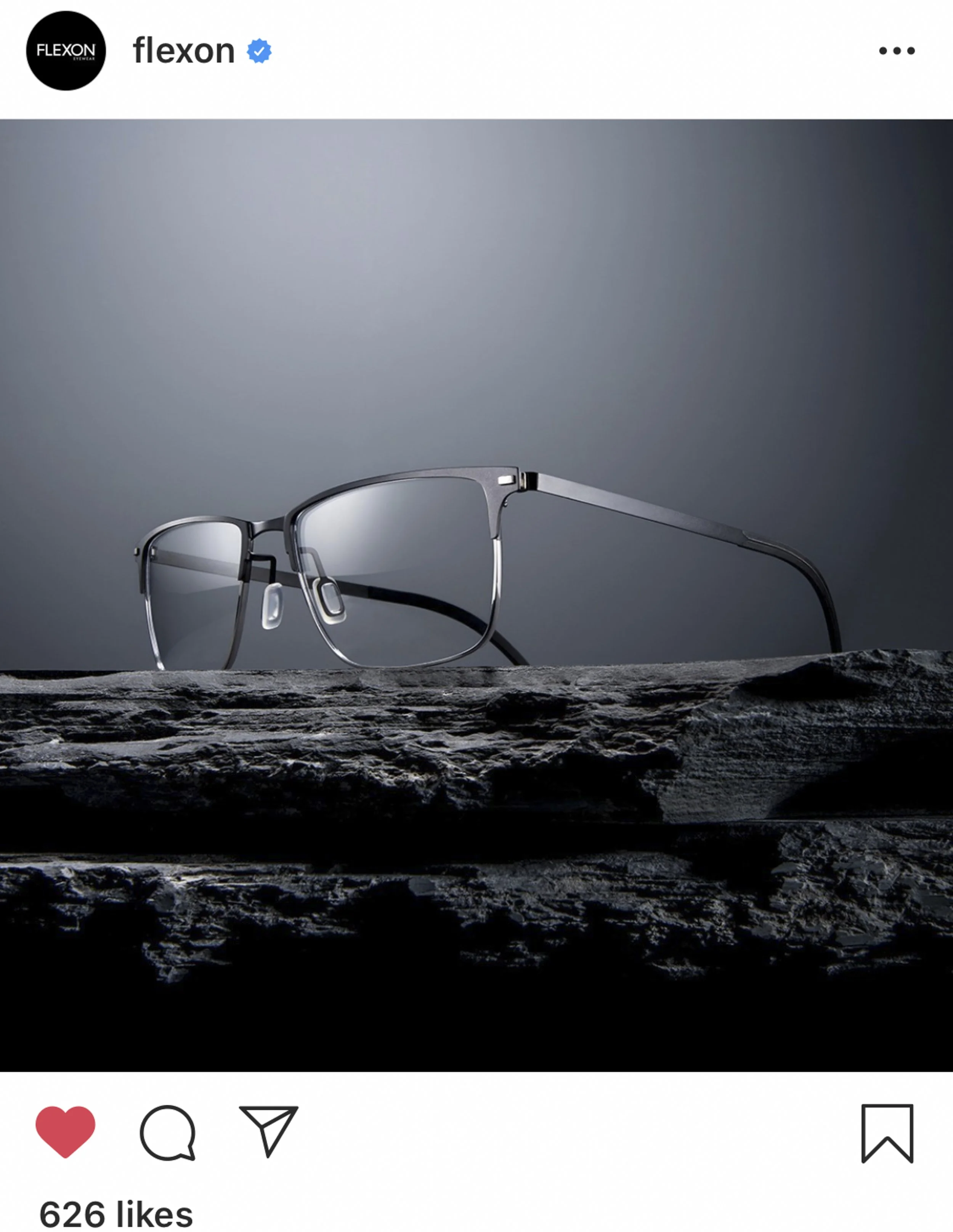 A pair of modern eyeglasses with metal frames resting on a textured dark surface, with a gray gradient background.