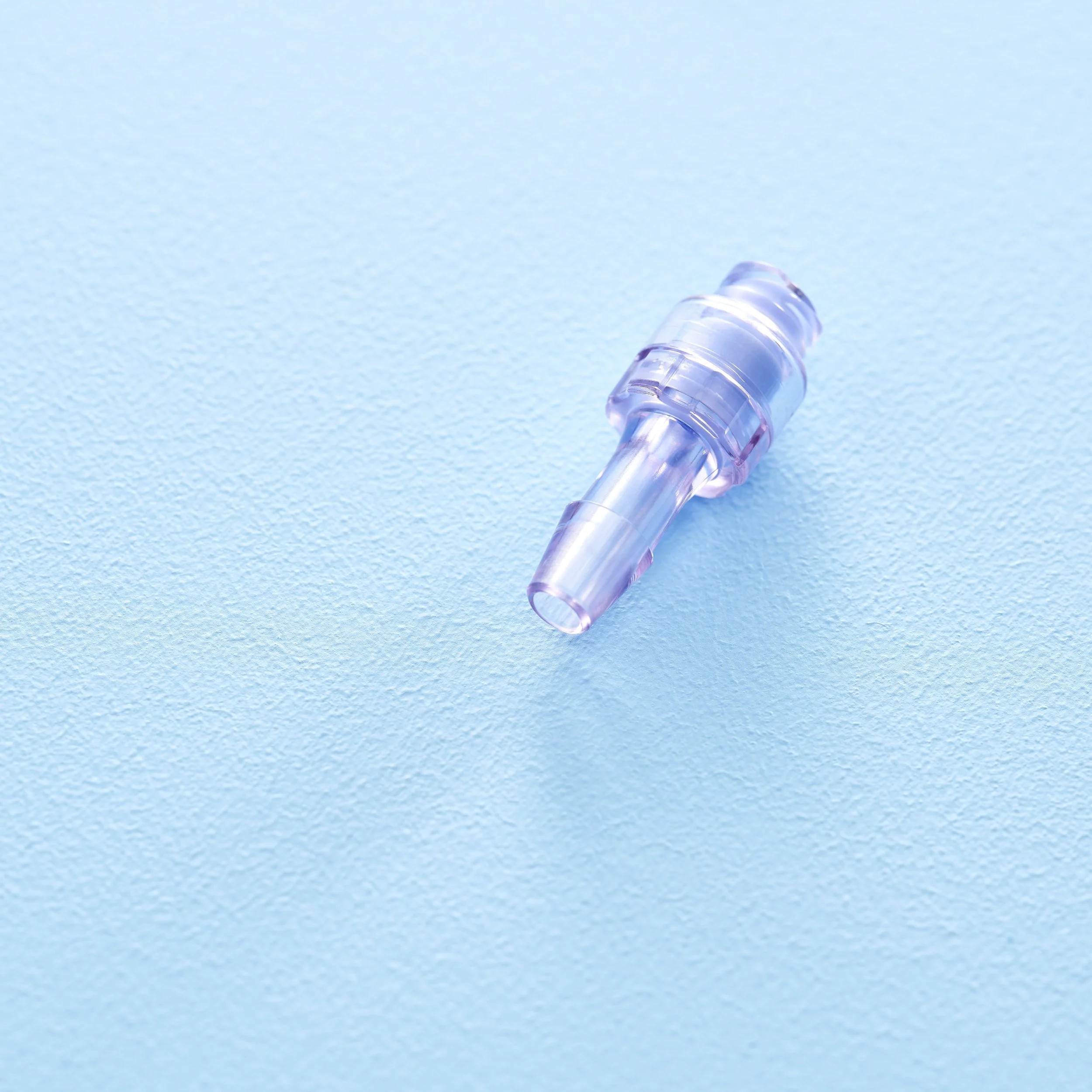 A translucent purple plastic nose clip lying on a textured light blue surface.