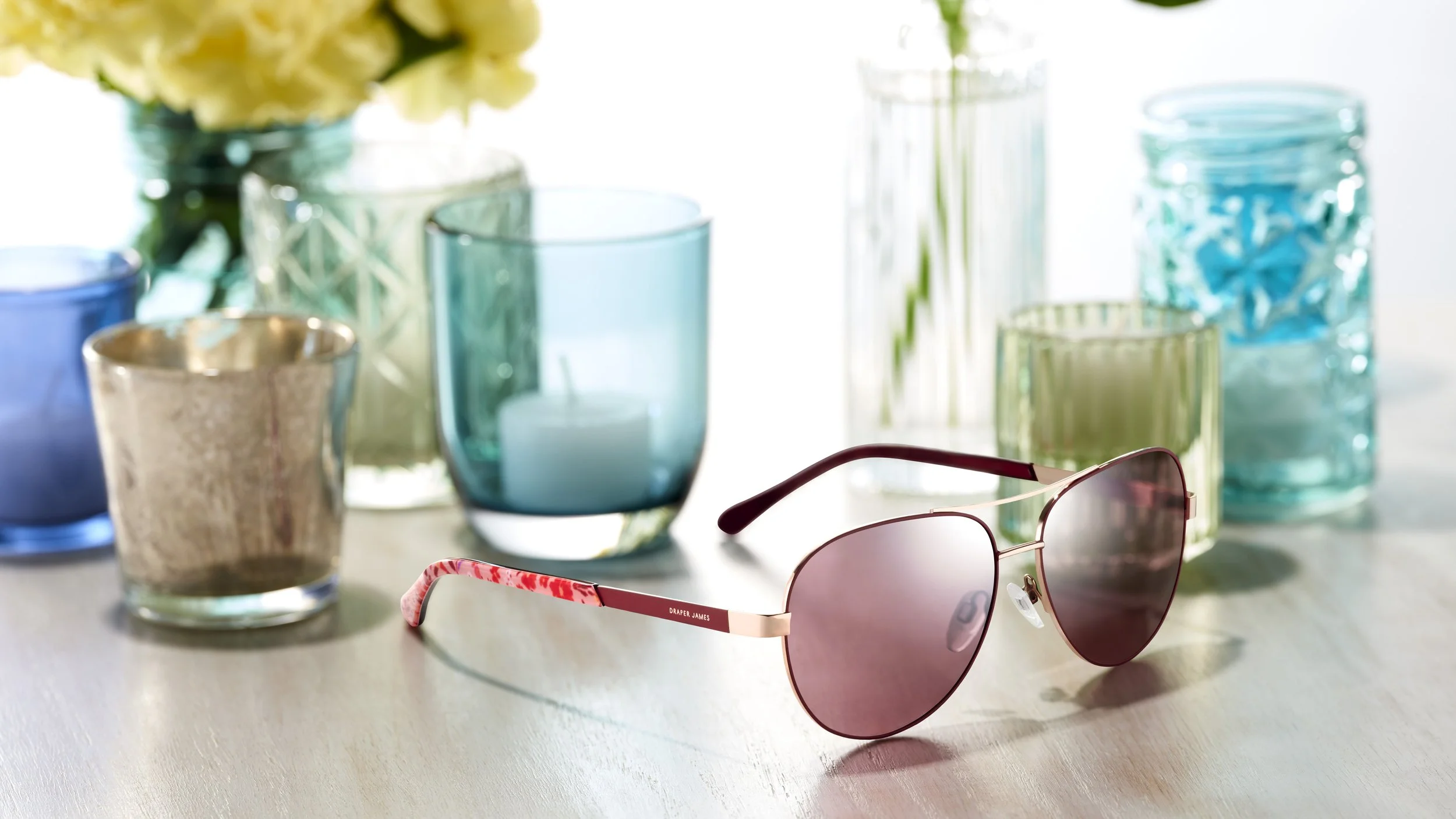 Colorful glass candle holders, vases, and sunglasses on a table.
