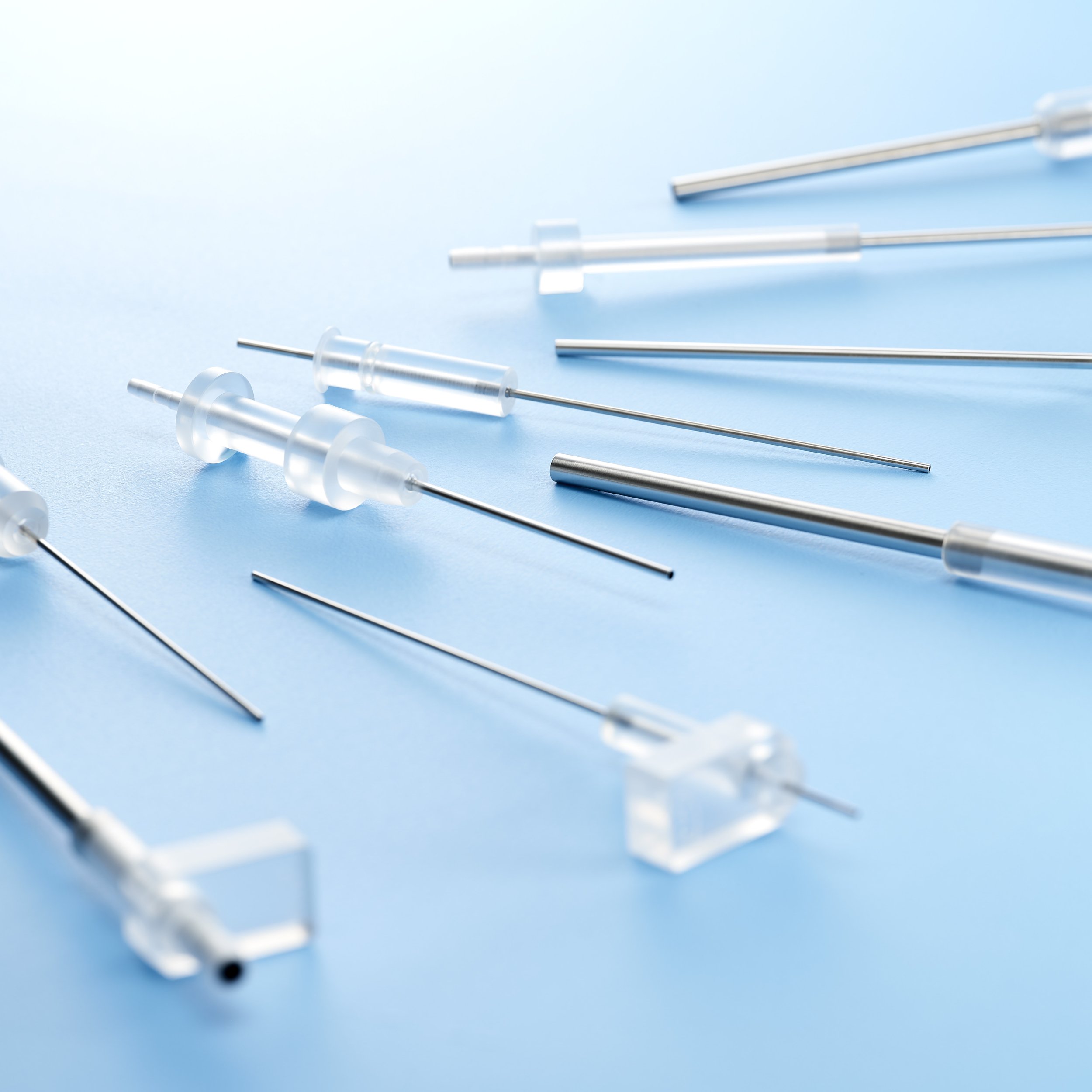 Collection of clear plastic and metal syringes on a blue background.