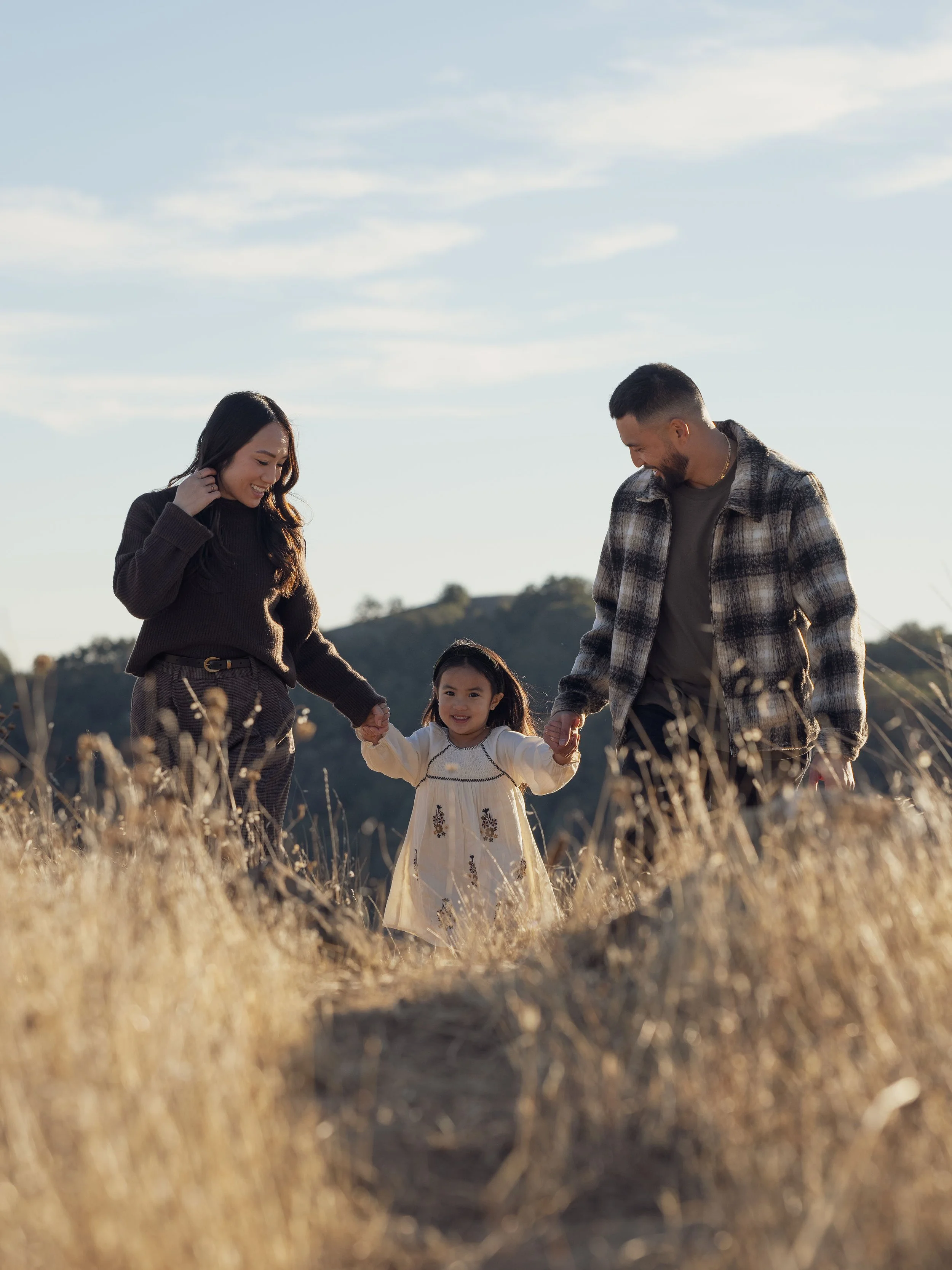Family portrait photography in golden hour lighting, showcasing a heartwarming moment in a natural setting. The image captures a serene family walk amidst tall grass, with soft focus and bokeh effect enhancing the aesthetic appeal.