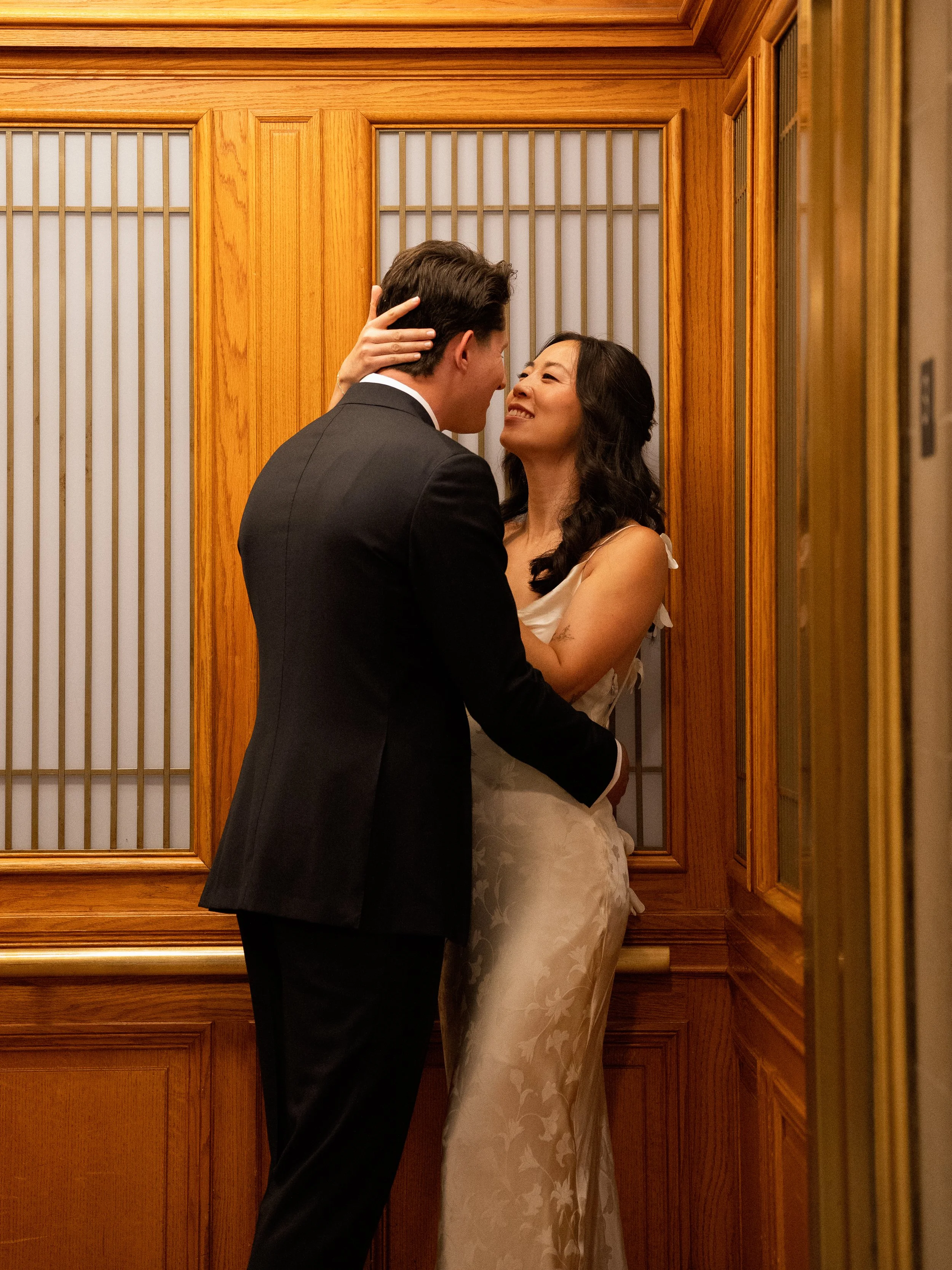 A couple in formal attire sharing an intimate moment in an elevator with wooden paneling.