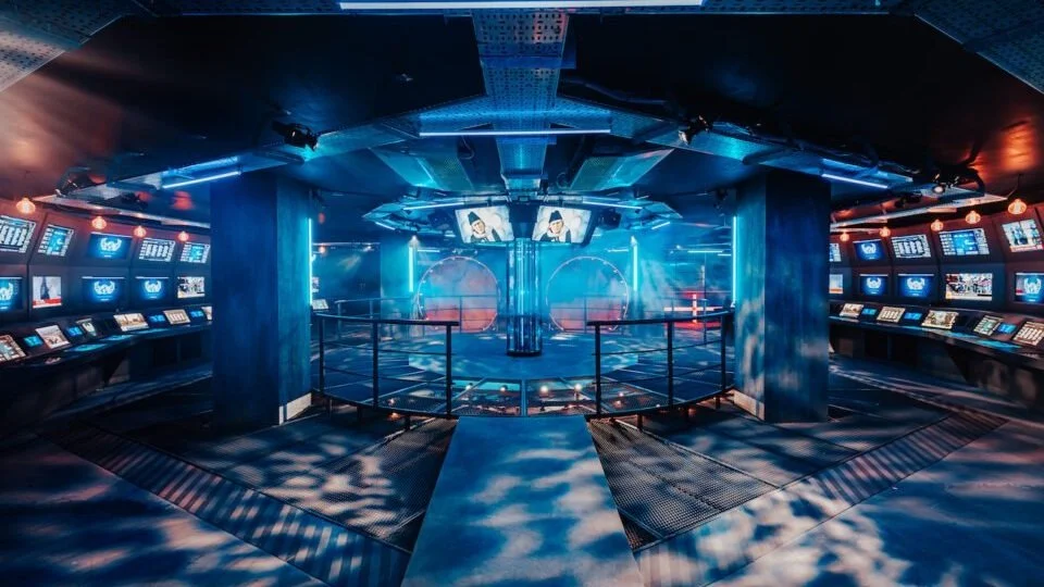 Interior of a futuristic arcade or gaming room with multiple screens and neon lighting.