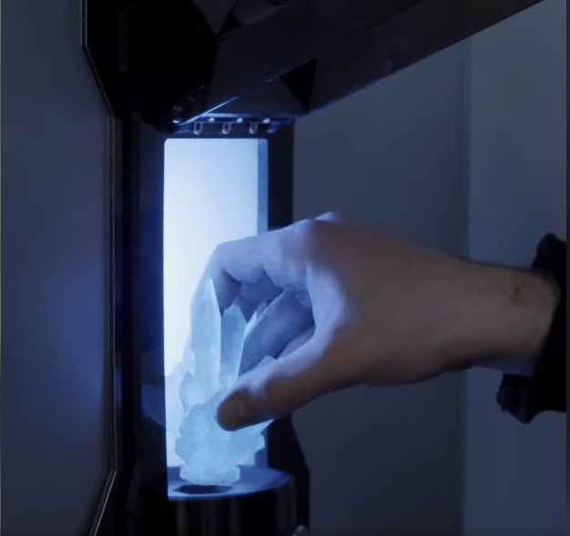 A hand placing a large crystal into a machine with a glowing blue light.