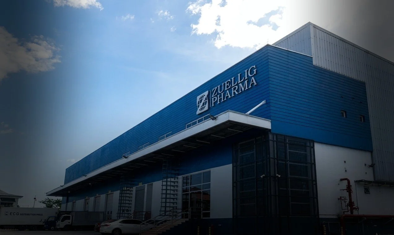 Exterior of a large pharmaceutical building with blue and gray panels, labeled 'Zuellig Pharma', under a partly cloudy sky.