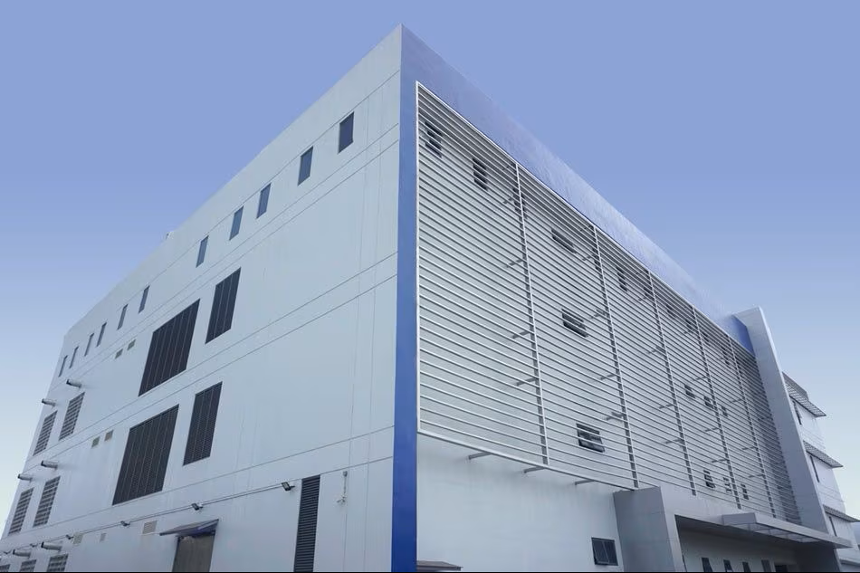 Front view of a modern, industrial-style building with large windows and metal louvers under a clear blue sky.