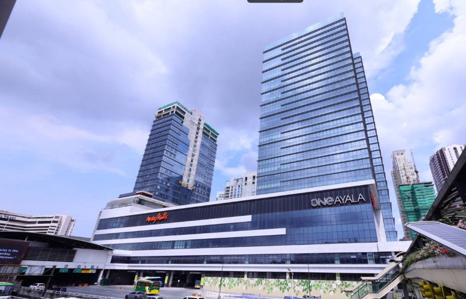 Modern high-rise office buildings and a shopping mall in an urban cityscape under a partly cloudy sky.