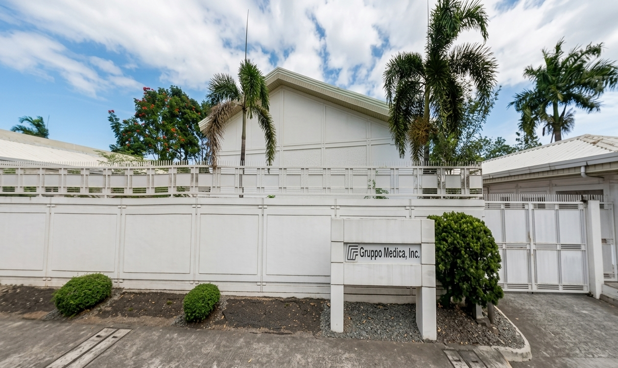 Exterior of a medical office building with white walls, palm trees, and a sign that reads 'Gruppo Medica, Inc.'
