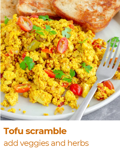 Scrambled tofu garnished with cherry tomatoes and herbs, served with toasted bread slices, on a white plate with a fork.