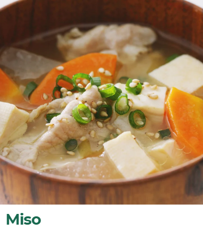 A bowl of miso soup with tofu, carrots, green onions, and chicken in a wooden bowl.