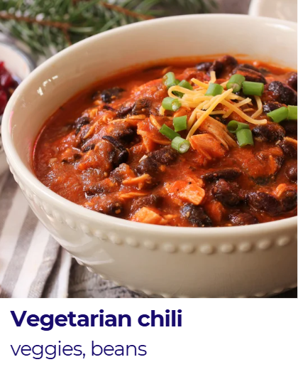 Bowl of vegetarian chili with beans, vegetables, topped with cheese and green onions.