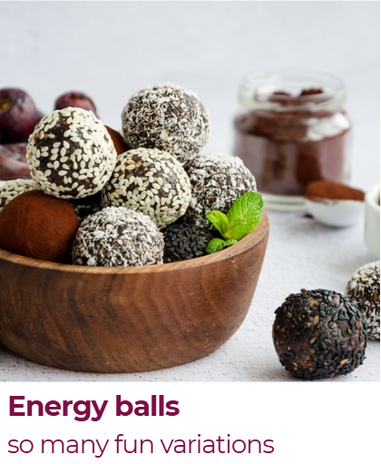 A wooden bowl filled with assorted energy balls, some coated in white or dark chocolate and sprinkled with seeds or coconut, with a jar of chocolate spread and a small spoon in the background.