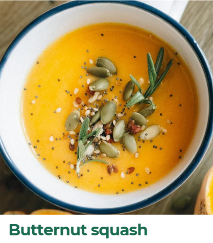 A bowl of bright orange butternut squash soup garnished with pumpkin seeds, sage leaves, and red pepper flakes.
