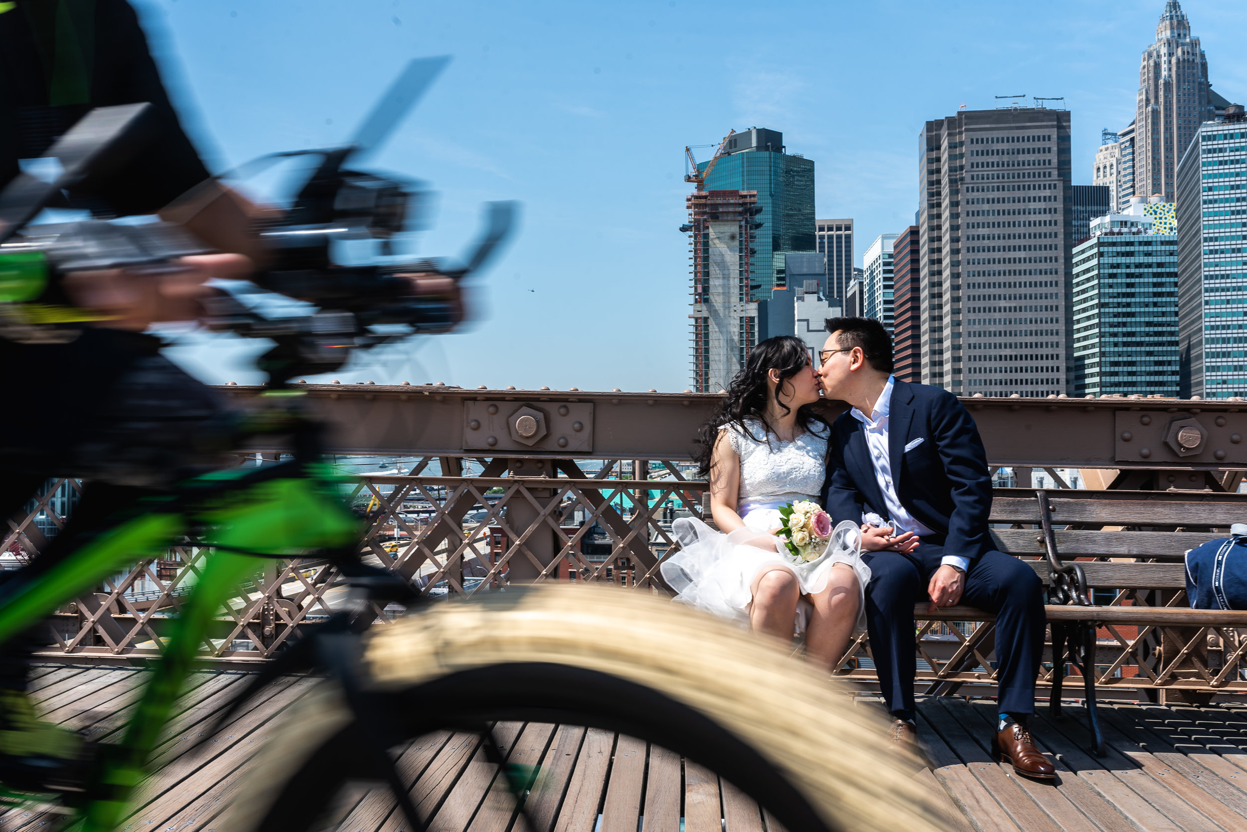 Bikes rolling past on the Brooklyn Bridge while the bride and groom kiss right after their City Hall Ceremony