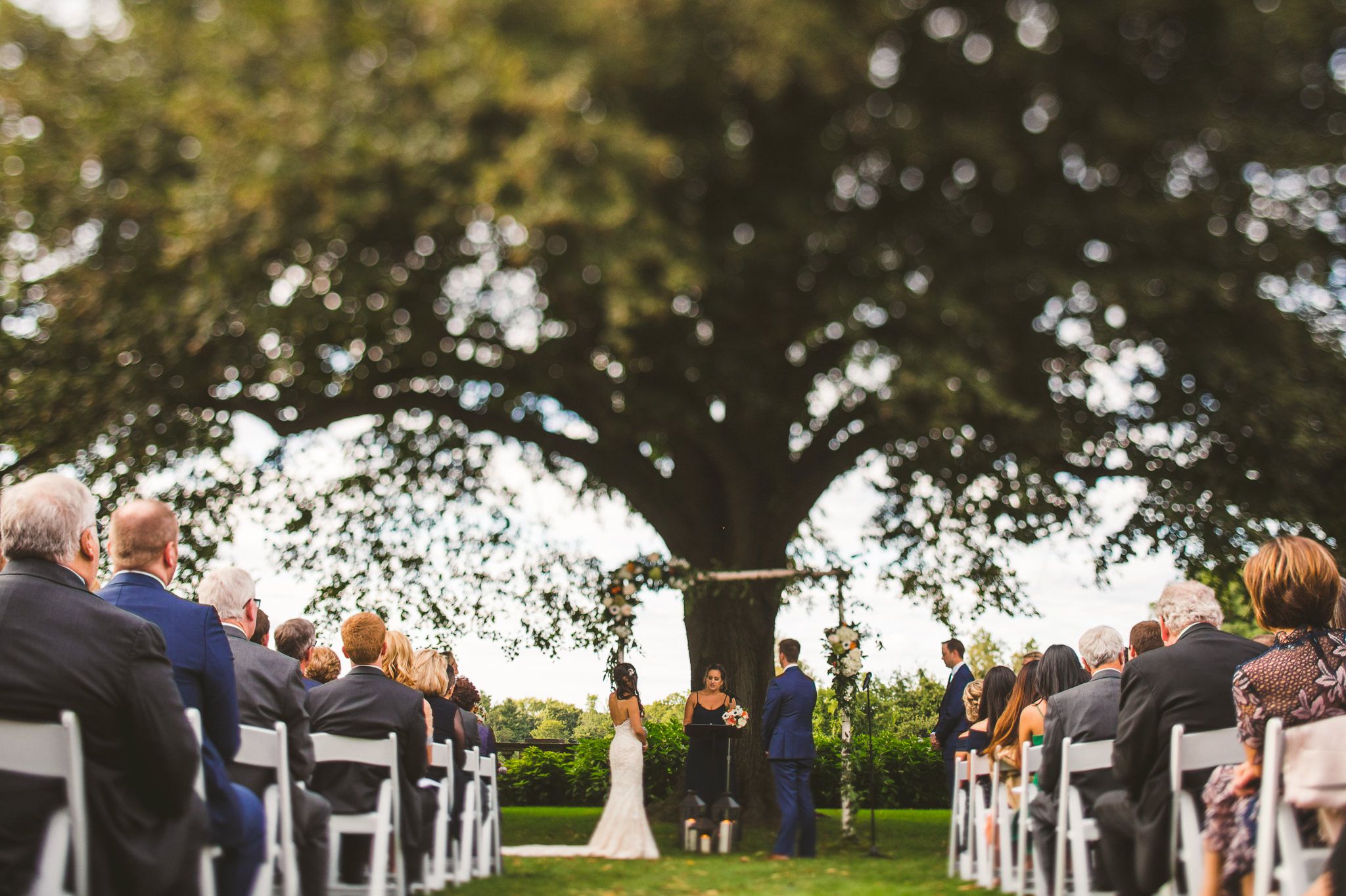  A tilt shift image taken of the ceremony as they listen to the officiant discuss marriage and vows. 

Scenes from Lisa and Colin's Long Island, New York Wedding at the New York Institute of Technology de Seversky Mansion.  