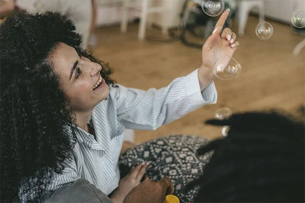 Woman smiling and pointing at soap bubbles, represents how you can better understand the different parts of yourself through IFS therapy.