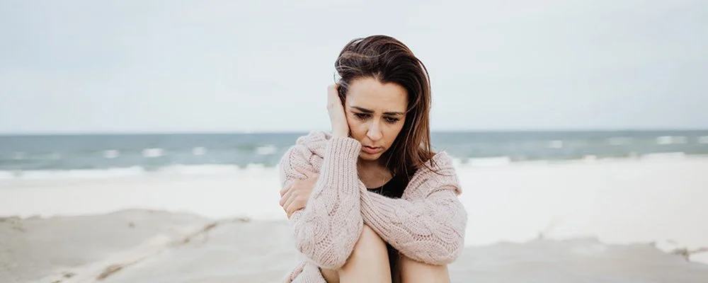 Woman sitting on a beach looking worried, represents how stress therapy in Los Angels can help you cope with stress.