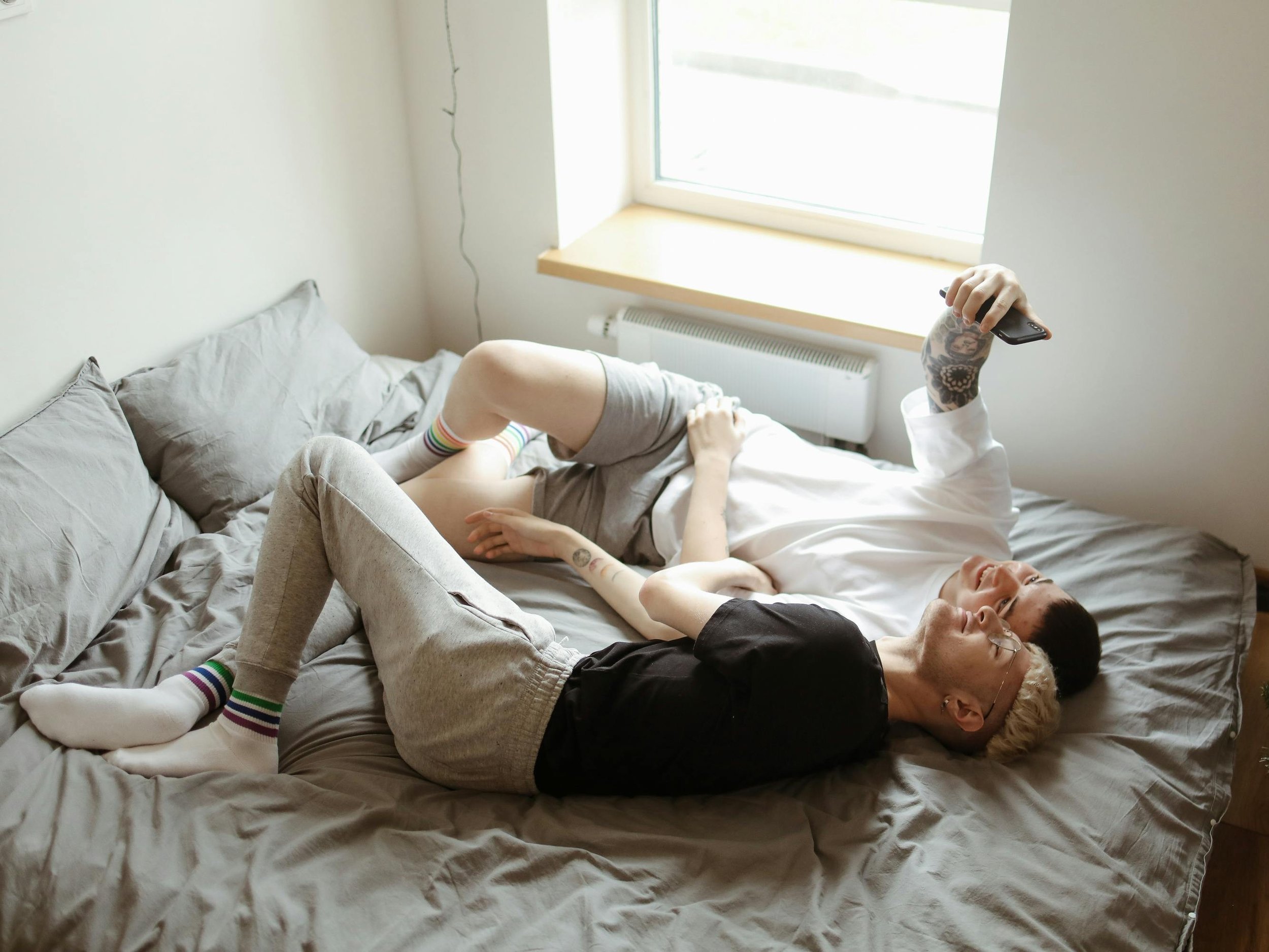 Two people lying together on a gray bed near a window in natural morning light