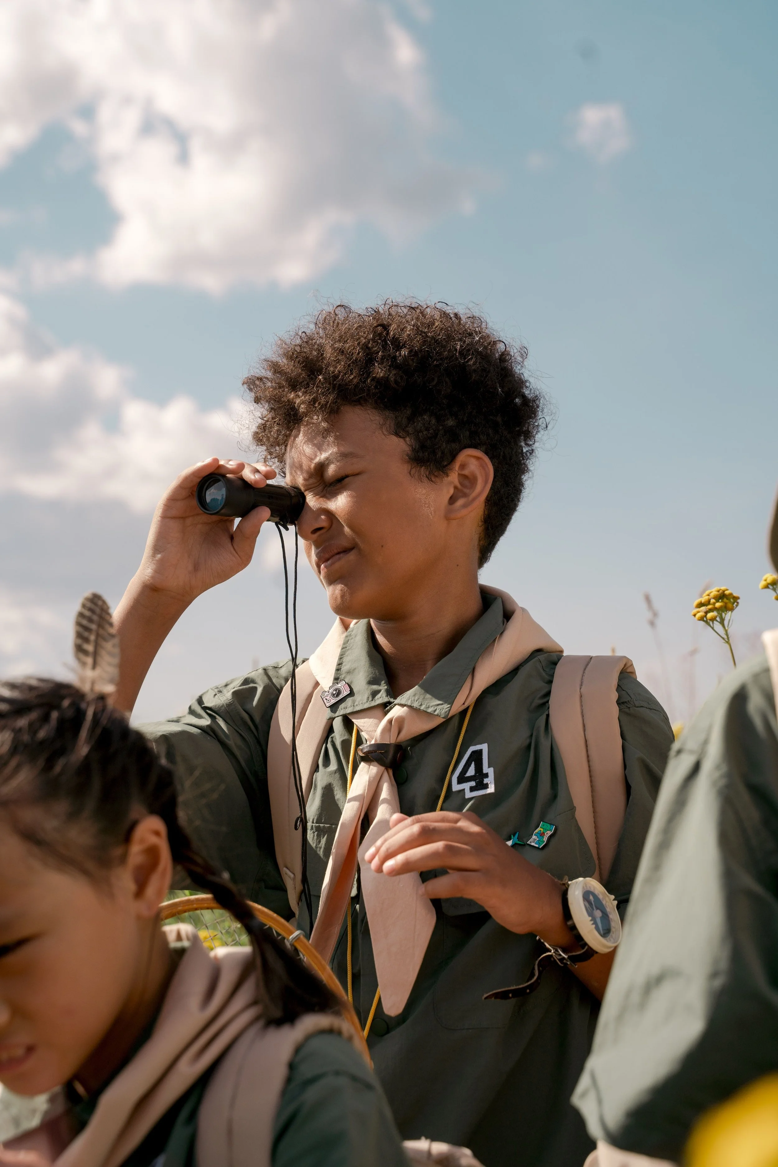 Child in scout uniform looking through binoculars during an outdoor family nature activity in Los Angeles