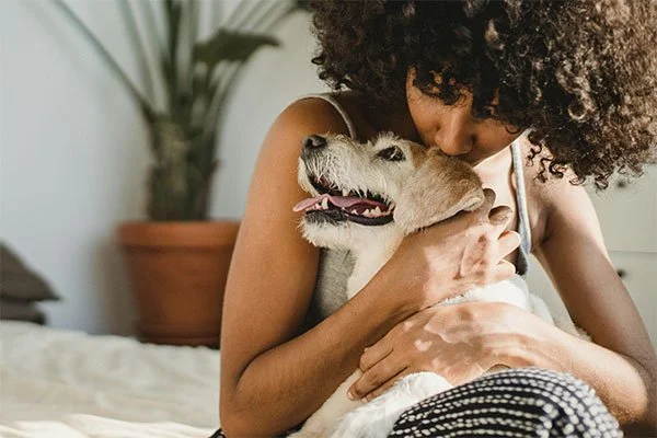 Woman kissing her dog, represents how working with an anxiety therapist can help you overcome anxiety challenges.