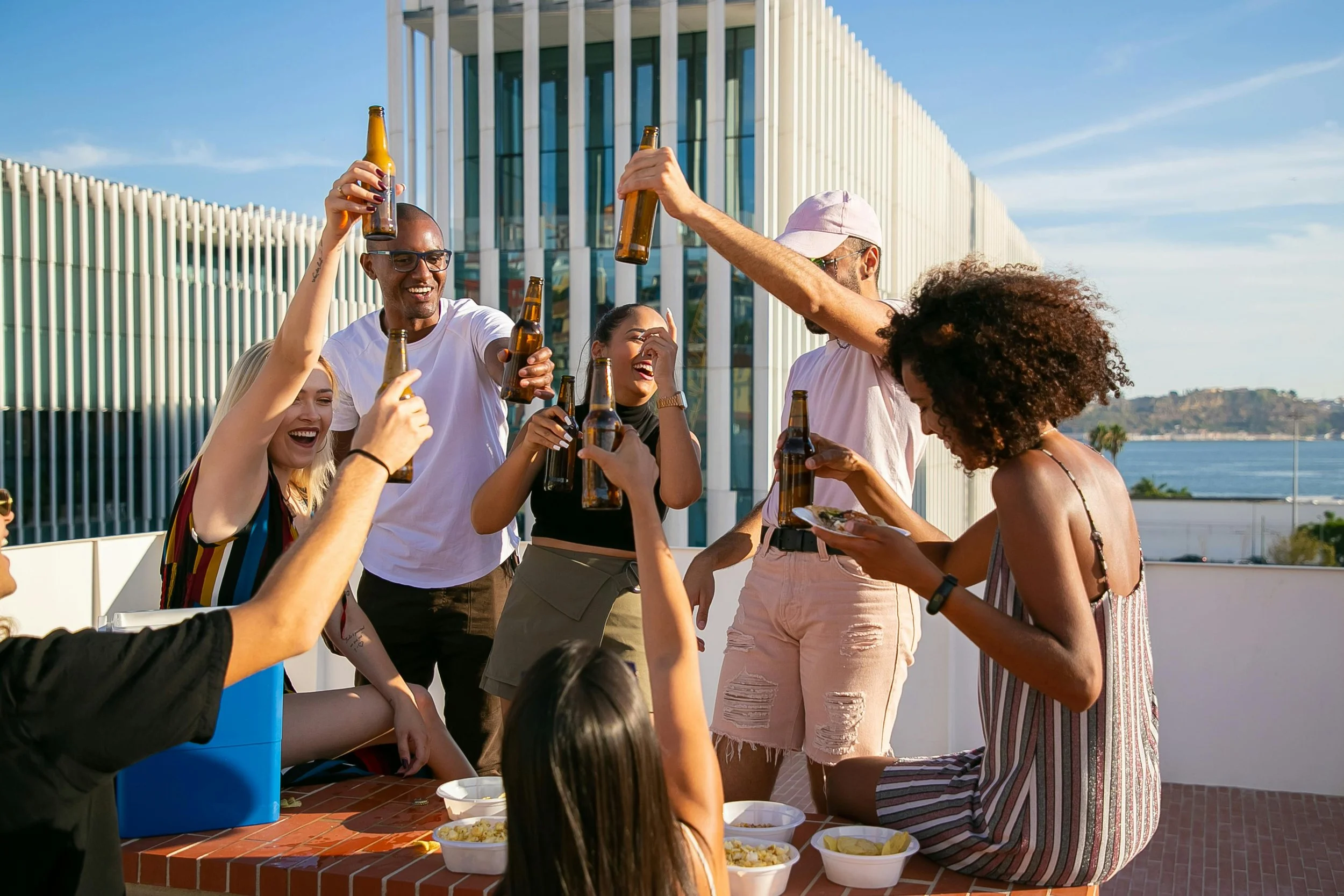 A diverse group of friends laughing and raising bottles together at an outdoor rooftop gathering in Los Angeles