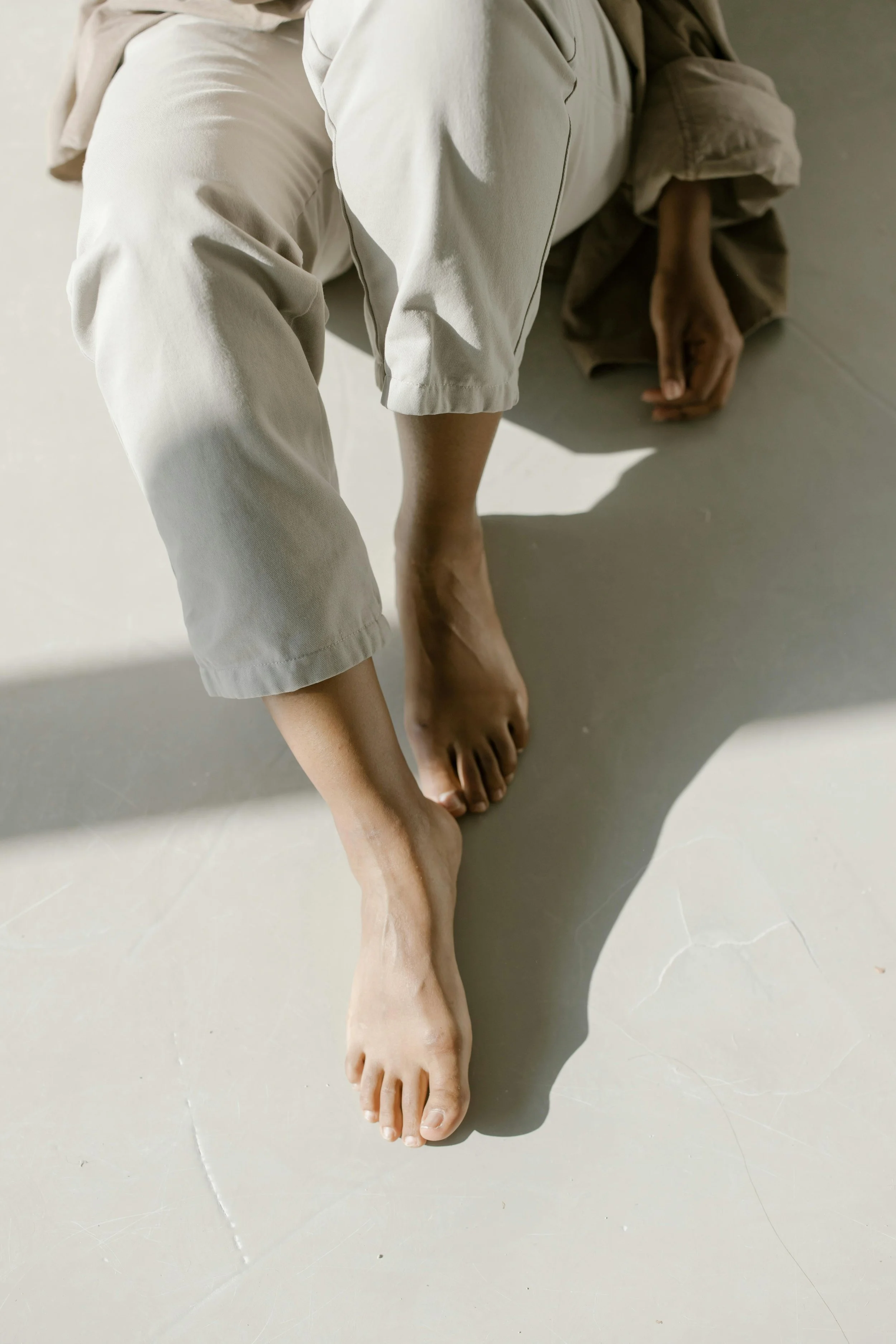 A person sitting on the floor with bare feet and knees drawn up, suggesting stillness, grounding, and the body's role in trauma healing