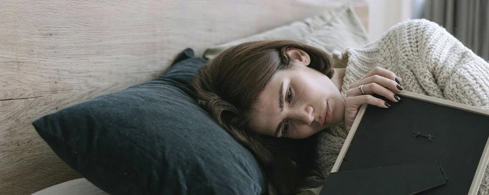 Woman in bed hugging a picture frame, represents how grief support in Los Angeles, CA, can help you find a life beyond loss.