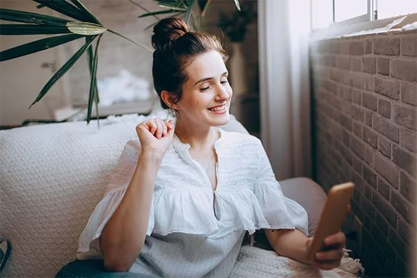 Woman sitting on a couch on a video call on her phone, represents the flexility of online counseling across LA and California.