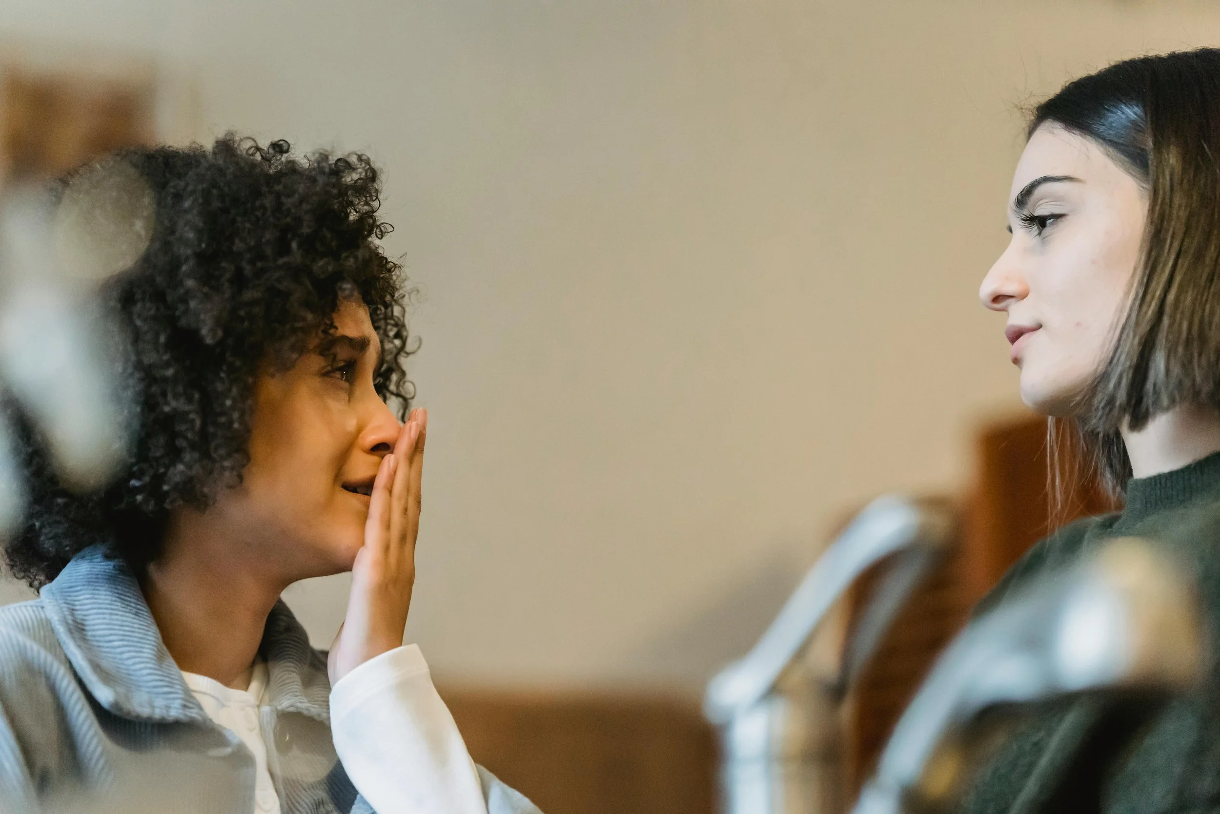 A woman crying while sharing something painful with a friend who listens with care