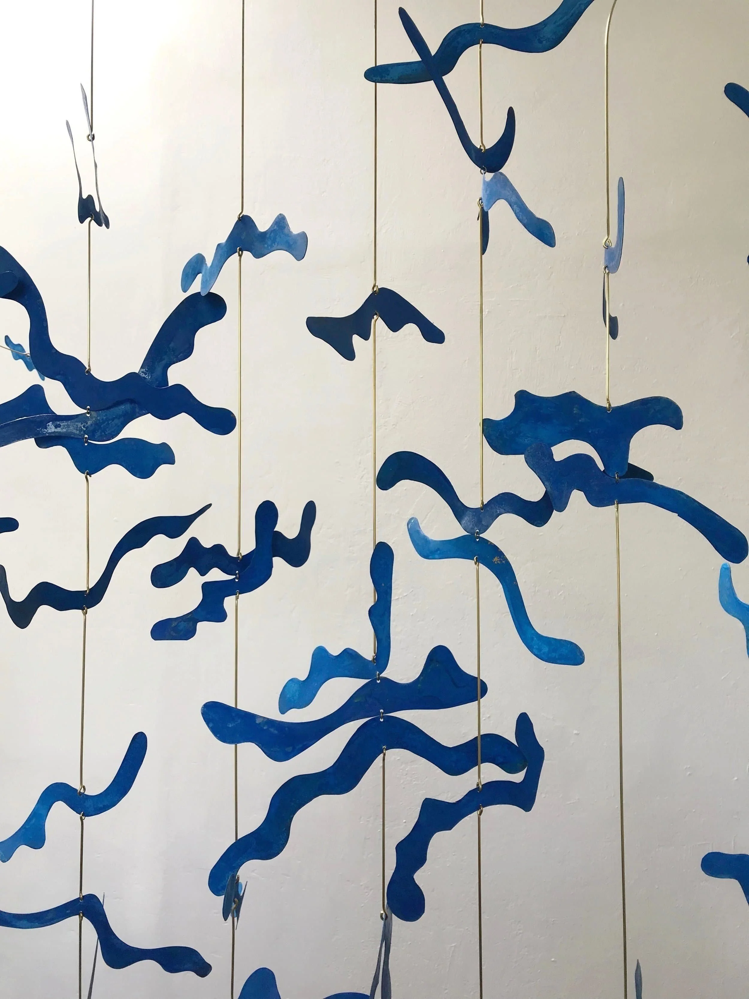 Blue abstract hanging art composed of wavy, irregular shapes suspended from thin vertical wires.