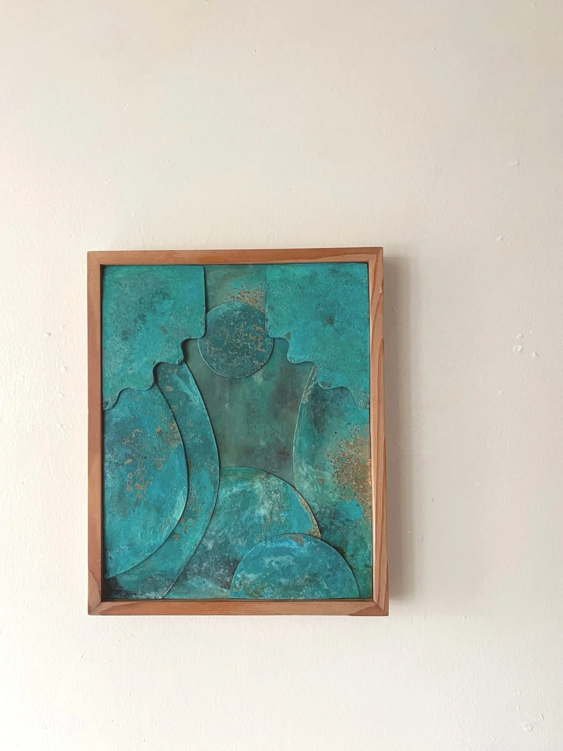 Abstract artwork with turquoise-colored verdigris patinated metal framed in wood on a white wall.