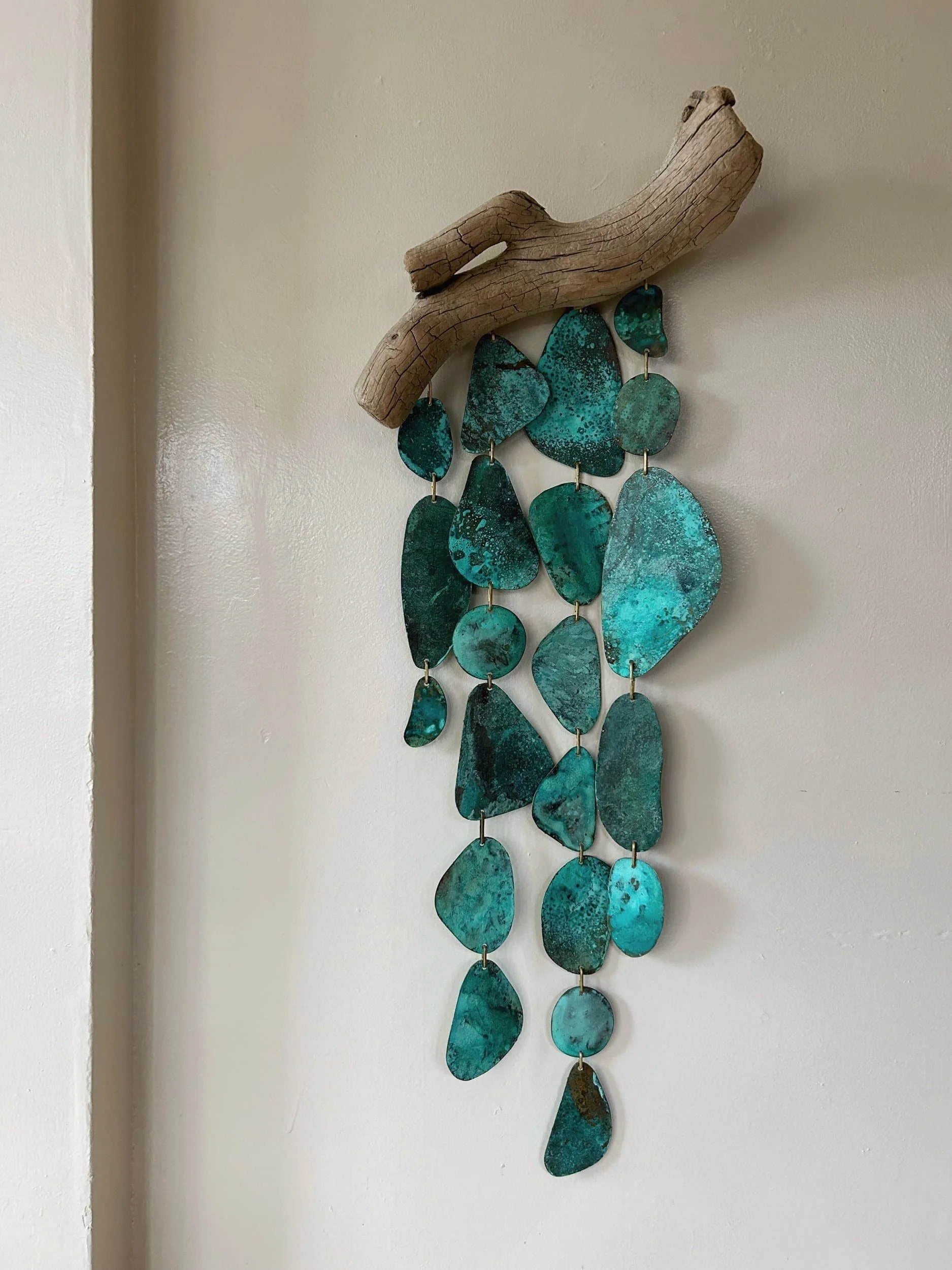 Decorative wall hanging made of driftwood and turquoise-colored verdigris patinated metal pieces.