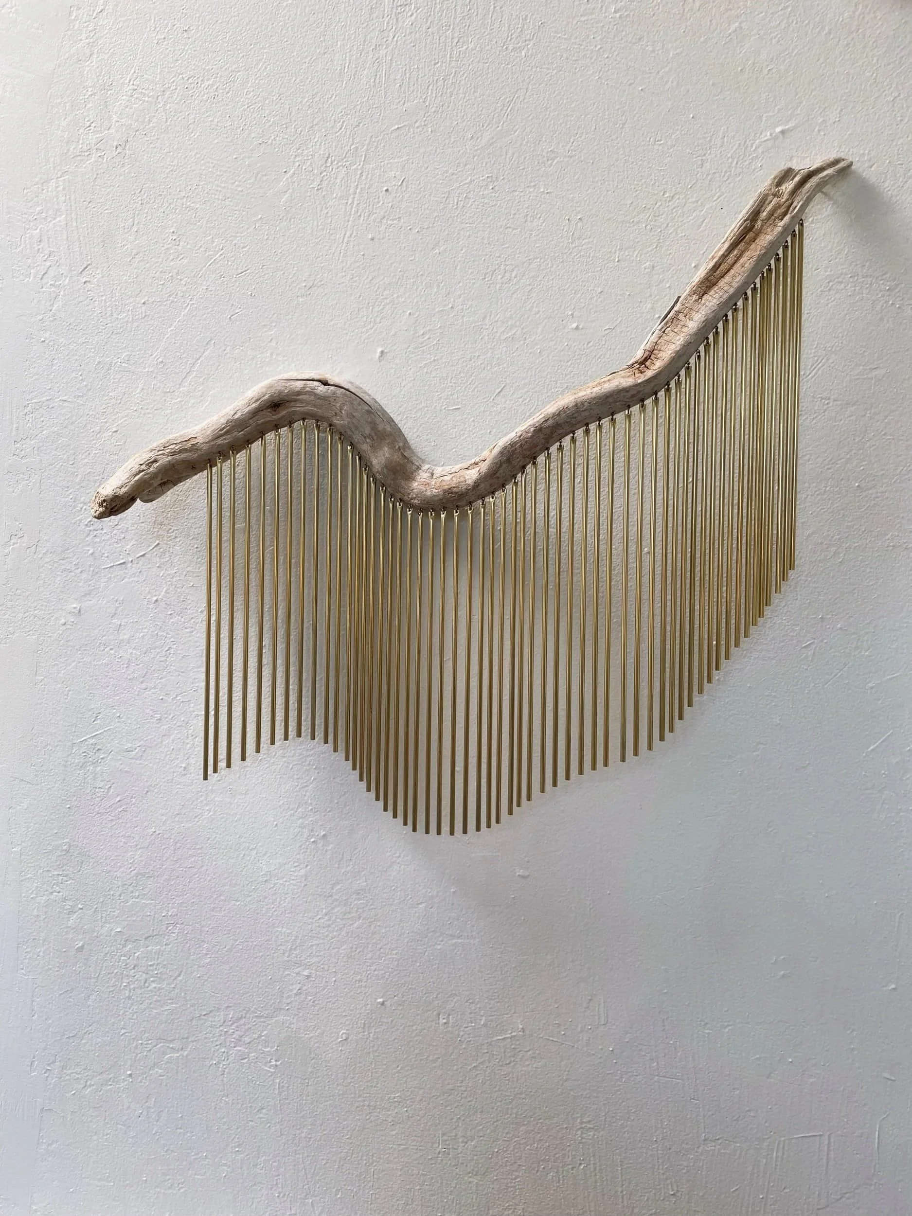 Decorative wall art made from a curved driftwood piece and vertical brass rods arranged in a wave pattern.