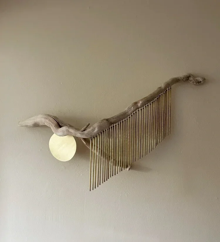 Decorative wall piece with a curved piece of driftwood, hanging brass tubing, with a brass sheet circle.