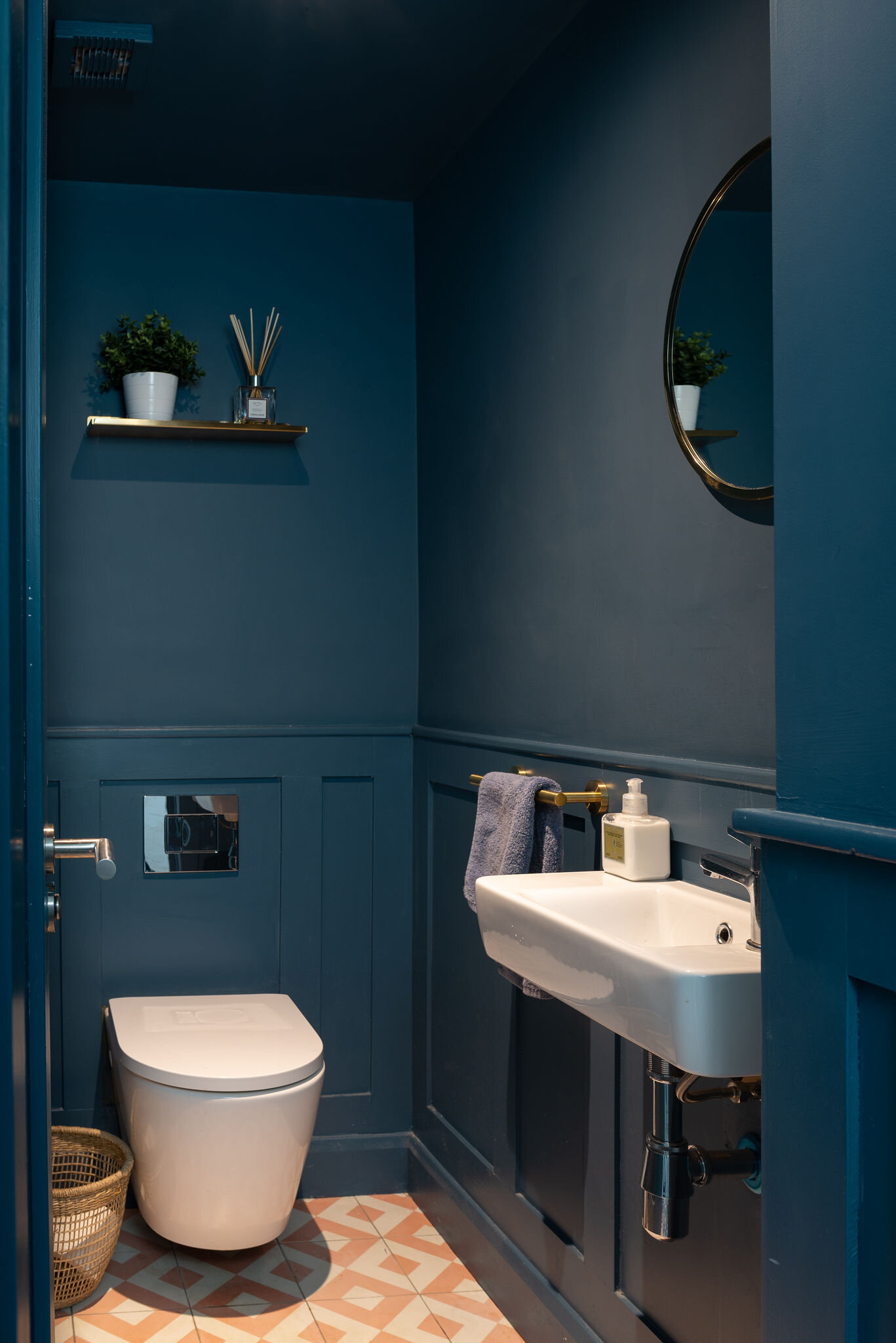 dark blue bathroom with floating sink and toilet and orange tile floor